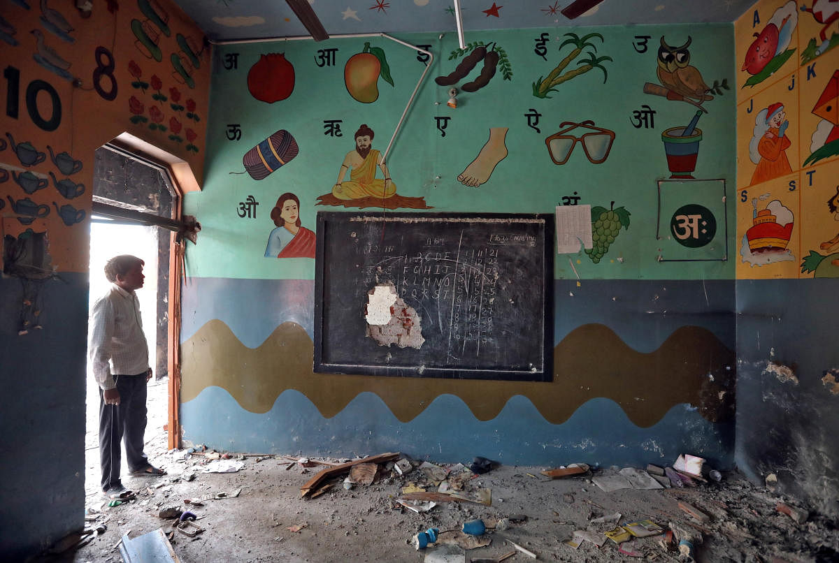 A man stands on the door of a partially damaged classroom after the school building was attacked by a mob in a riot affected area following clashes between people demonstrating for and against a new citizenship law in New Delhi