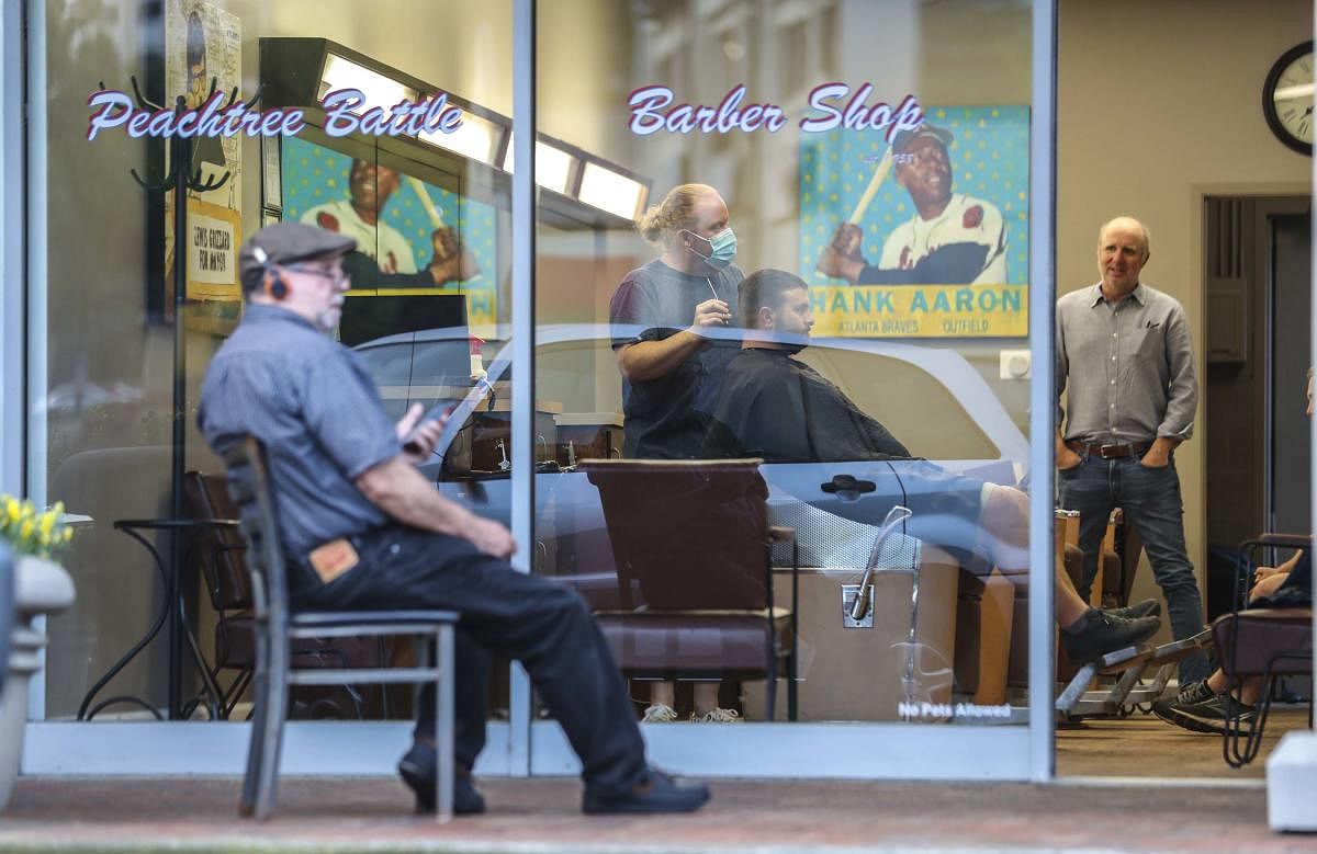 Barber and owner of Chris Edwards wears a mask and cuts the hair of customer as others wait at Peachtree Battle Barber Shop in Atlanta. AP/PTI