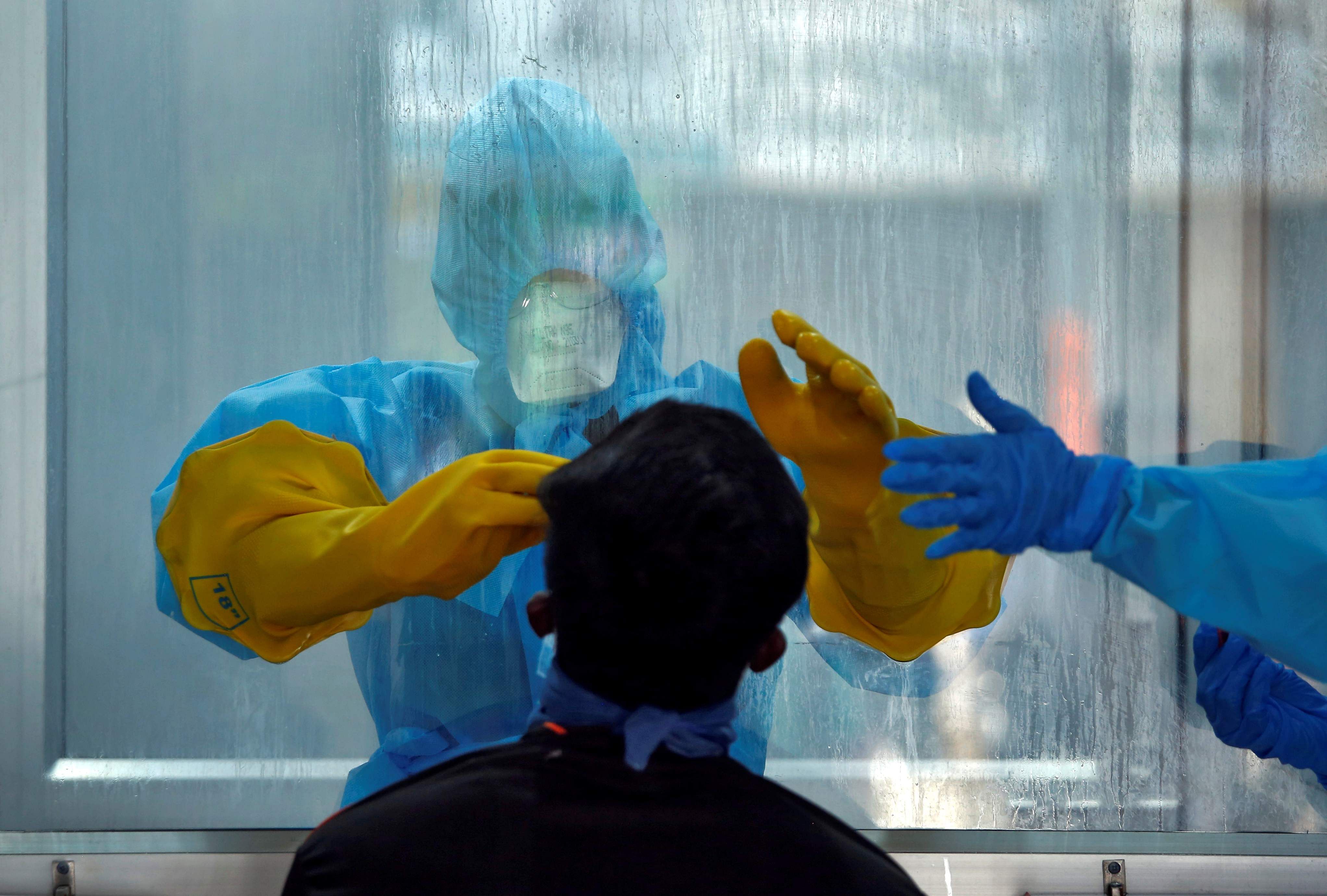 A doctor in a protective chamber takes a swab from a man to test for coronavirus disease (COVID-19) at a newly installed Walk-In Sample Kiosk (WISK) in a government-run hospital in Chennai. (Credit: Reuters)