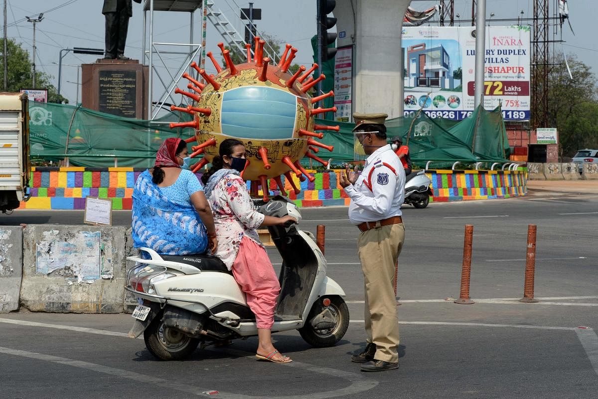 A traffic police officer (R) stands infront of a coronavirus-themed globe at a traffic junction enquire people travel during coronavirus (AFP Photo)