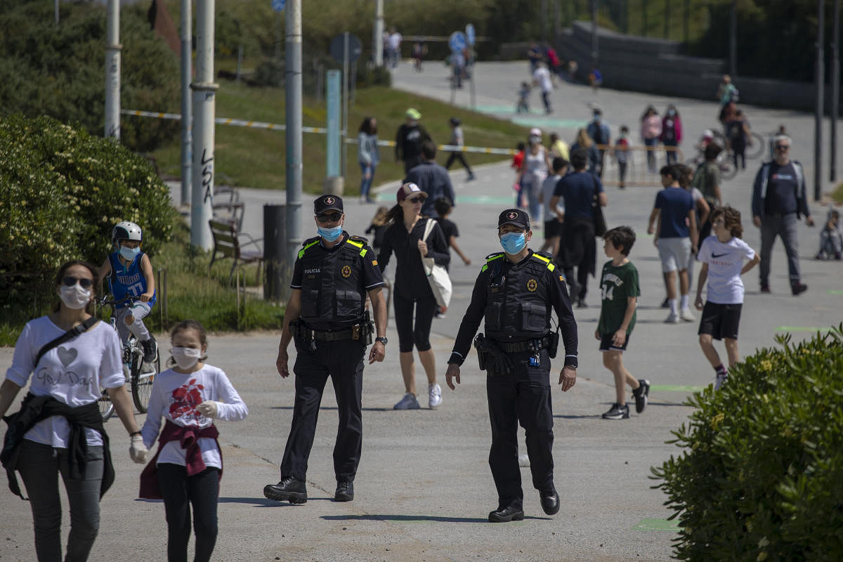 Catalan police officers patrol as families with their children walk along a boulevard in Barcelona, Spain, Sunday, April 26, 2020 as the lockdown to combat the spread of coronavirus continues. Credit: AP Photo