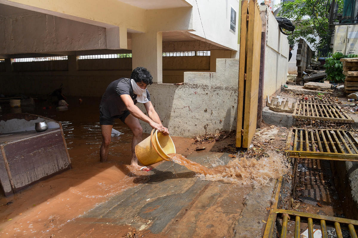 A resident flushes out dirty rainwater from the basement of the Deccan Heritage apartment in ITI Layout, New BEL Road, in Bengaluru on Friday. DH PHOTO/B H SHIVAKUMAR