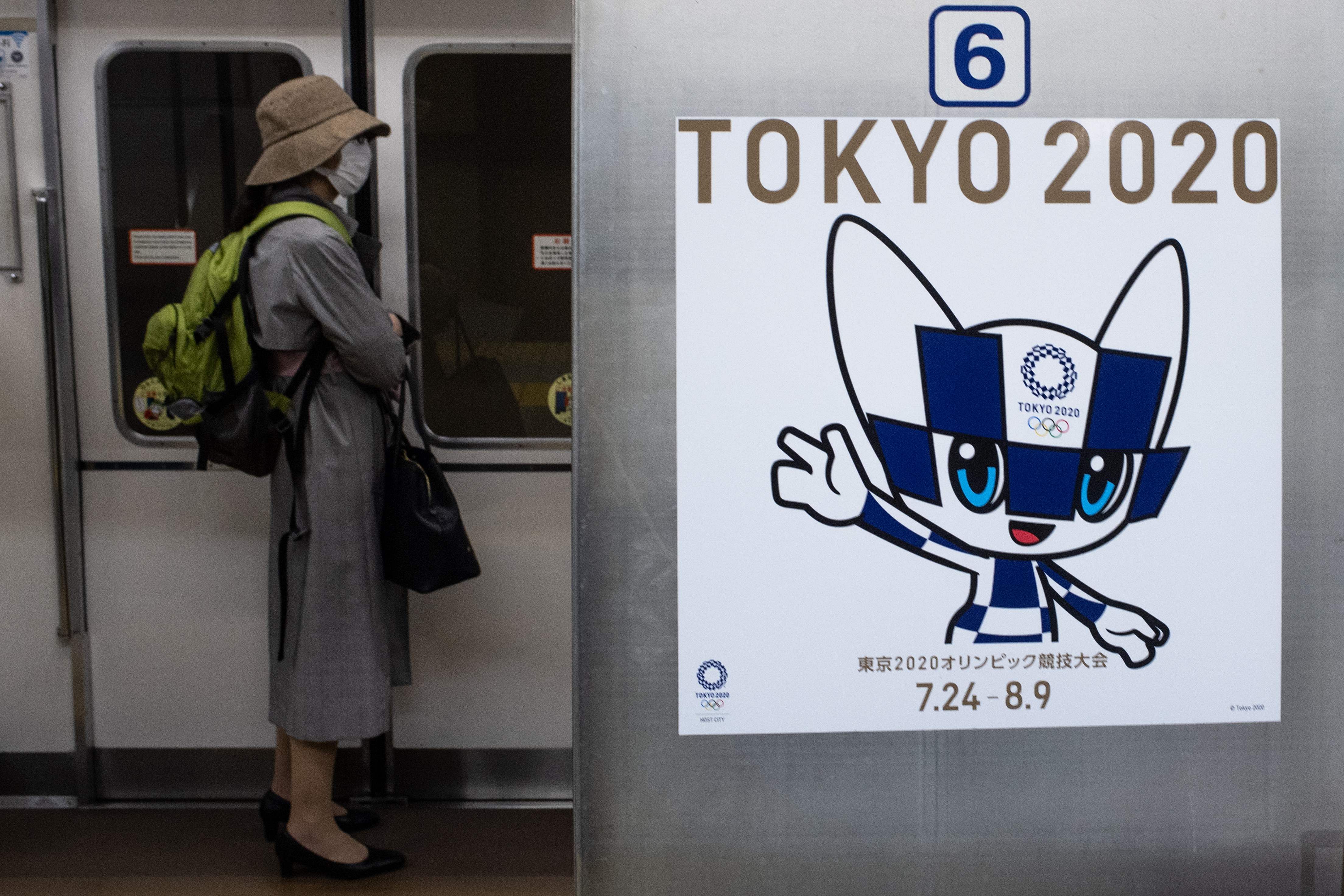 A passenger wearing a face mask stands next to a poster of Tokyo 2020 Olympic mascot Miraitowa on a train in Tokyo. (AFP photo)