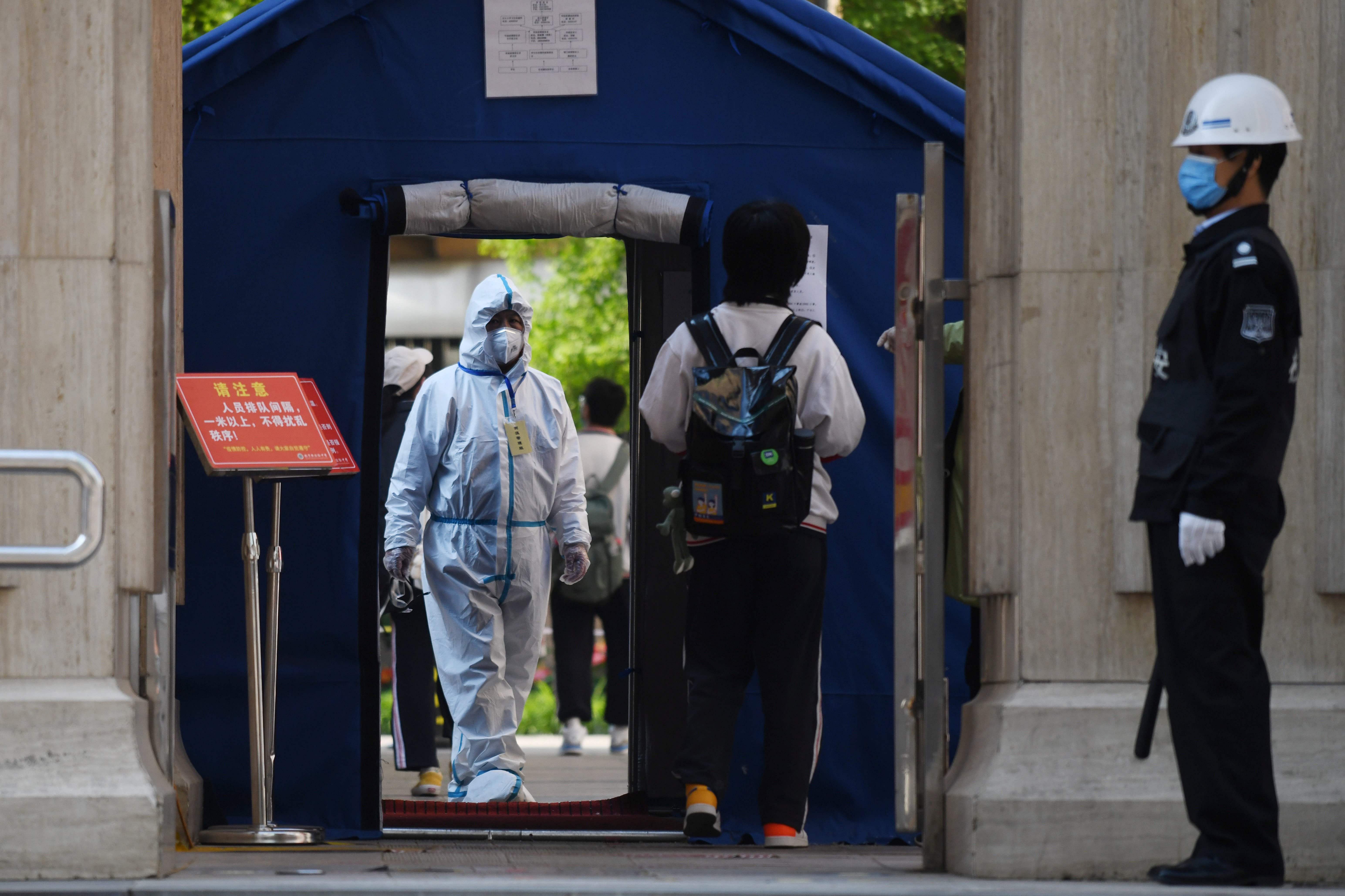 An official in a hazmat suit waits inside a high school entrance as a student arrives in Beijing. (AFP Photo)