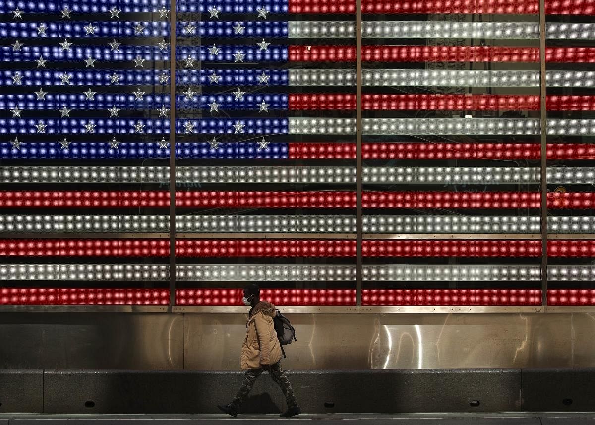 A pedestrian, wearing a protective face mask walks past the American flag video board (AFP Photo)
