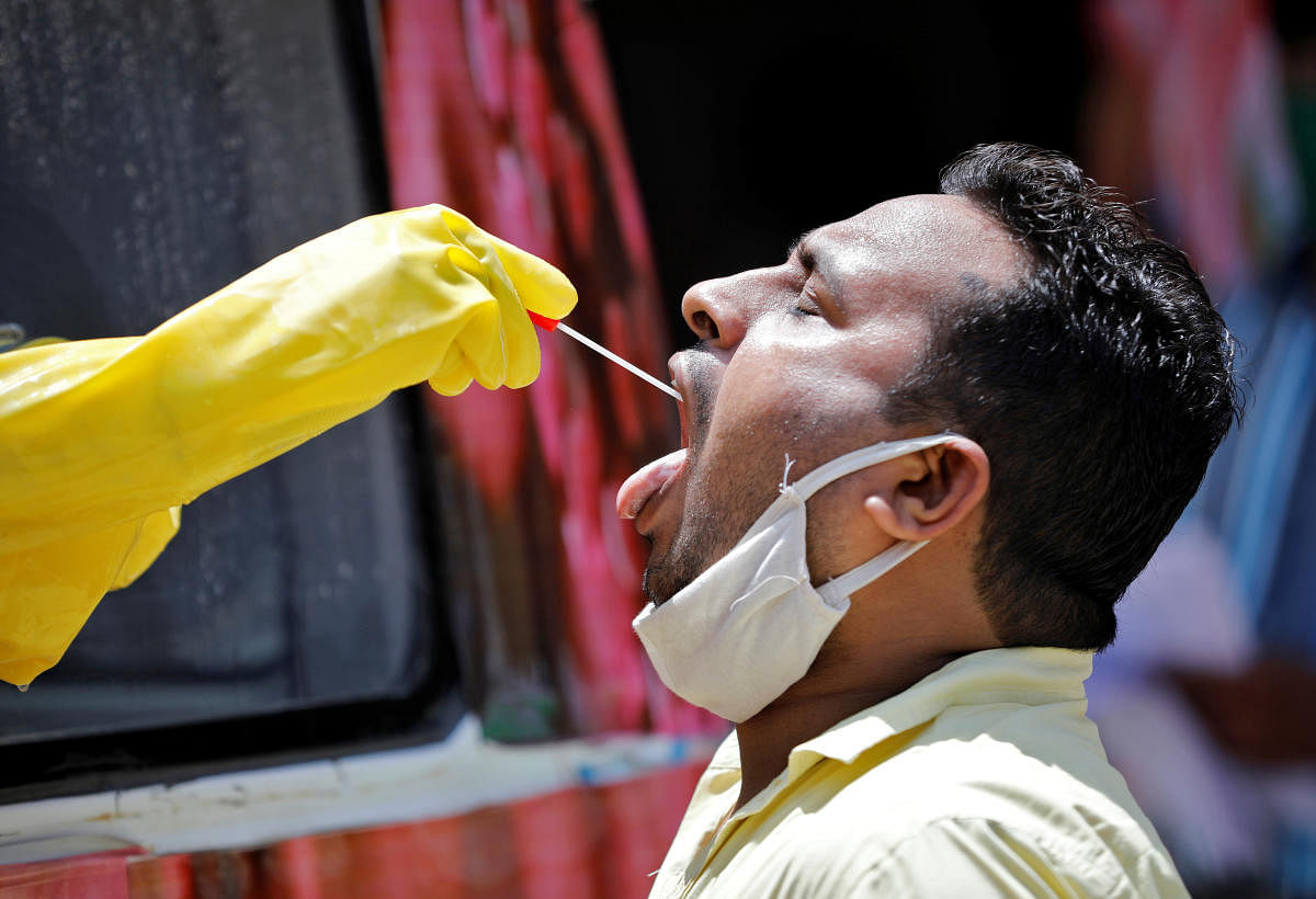 A medical worker sitting inside a mobile test van for the coronavirus disease (COVID-19) takes a swab from a man to test for the disease, on the outskirts of Ahmedabad, India, April 27, 2020. Credit: Reuters Photo