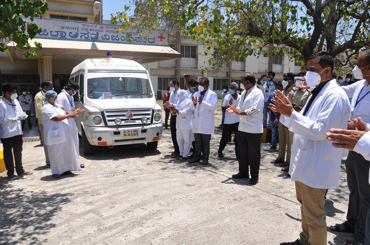 Doctors and other medical staff clap as the vehicle ferrying the first Covid-19 recovered patient leaves district hospital in Vijayapura on Sunday. DH Photo