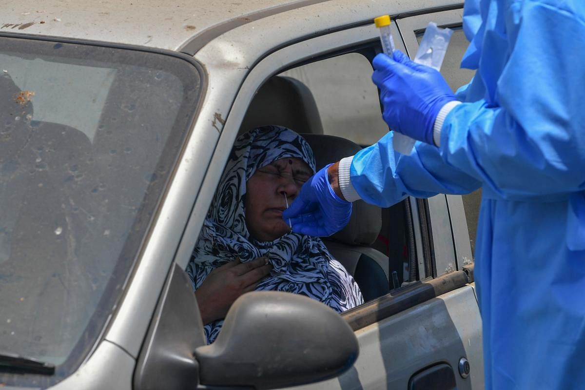 A doctor (R) collects a nasal swab from a woman sitting inside a car at a Drive-thru Collection Point Test Centre during a government-imposed nationwide lockdown as a preventive measure against the spread of the COVID-19 coronavirus in Mumbai on April 27, 2020. Credit: AFP Photo