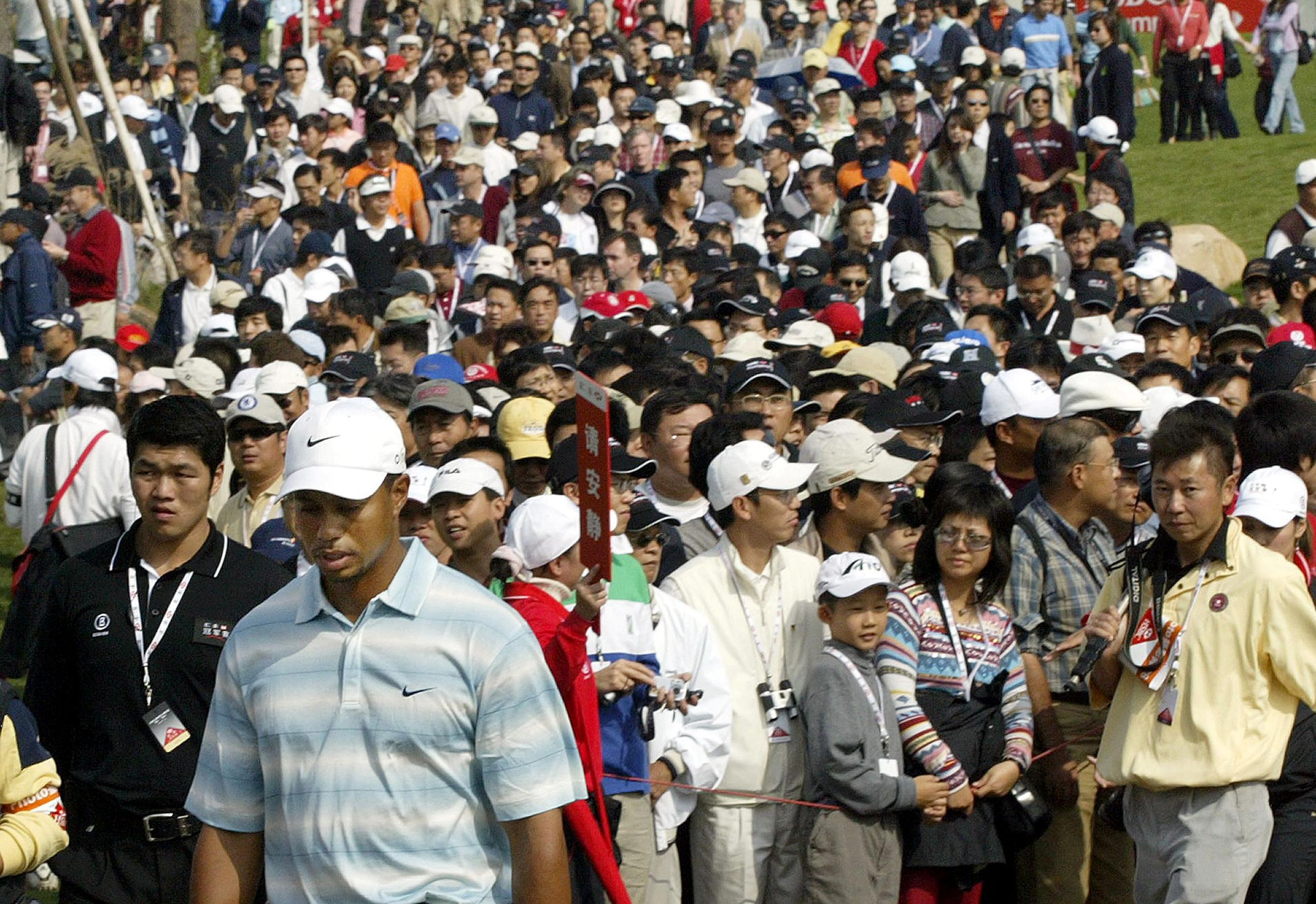 This file photo taken on November 12, 2005 shows US golfer Tiger Woods (front L, in white hat) being followed by a large crowd of Chinese spectators as he walks from the tee-off area during the HSBC Champions golf tournament in Shanghai. (Credit: AFP)
