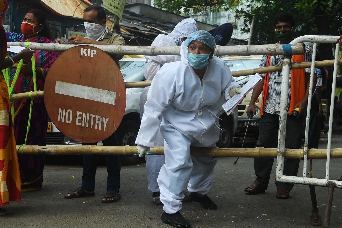 A municipal worker wearing a hazmat suits crosses a barrier during a door to door survey on residential area during a government-imposed nationwide lockdown as a preventive measure against the COVID-19 coronavirus, in Kolkata on April 29, 2020. Credit: AFP Photo