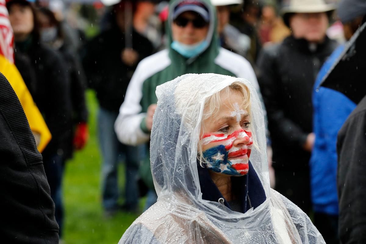 A protestor with an upside down flag painted on her face stands at an American Patriot Rally organized by Michigan United for Liberty protest for the reopening of businesses, on the steps of the Michigan State Capitol in Lansing, Michigan on April 30, 2020. Credit: AFP Photo