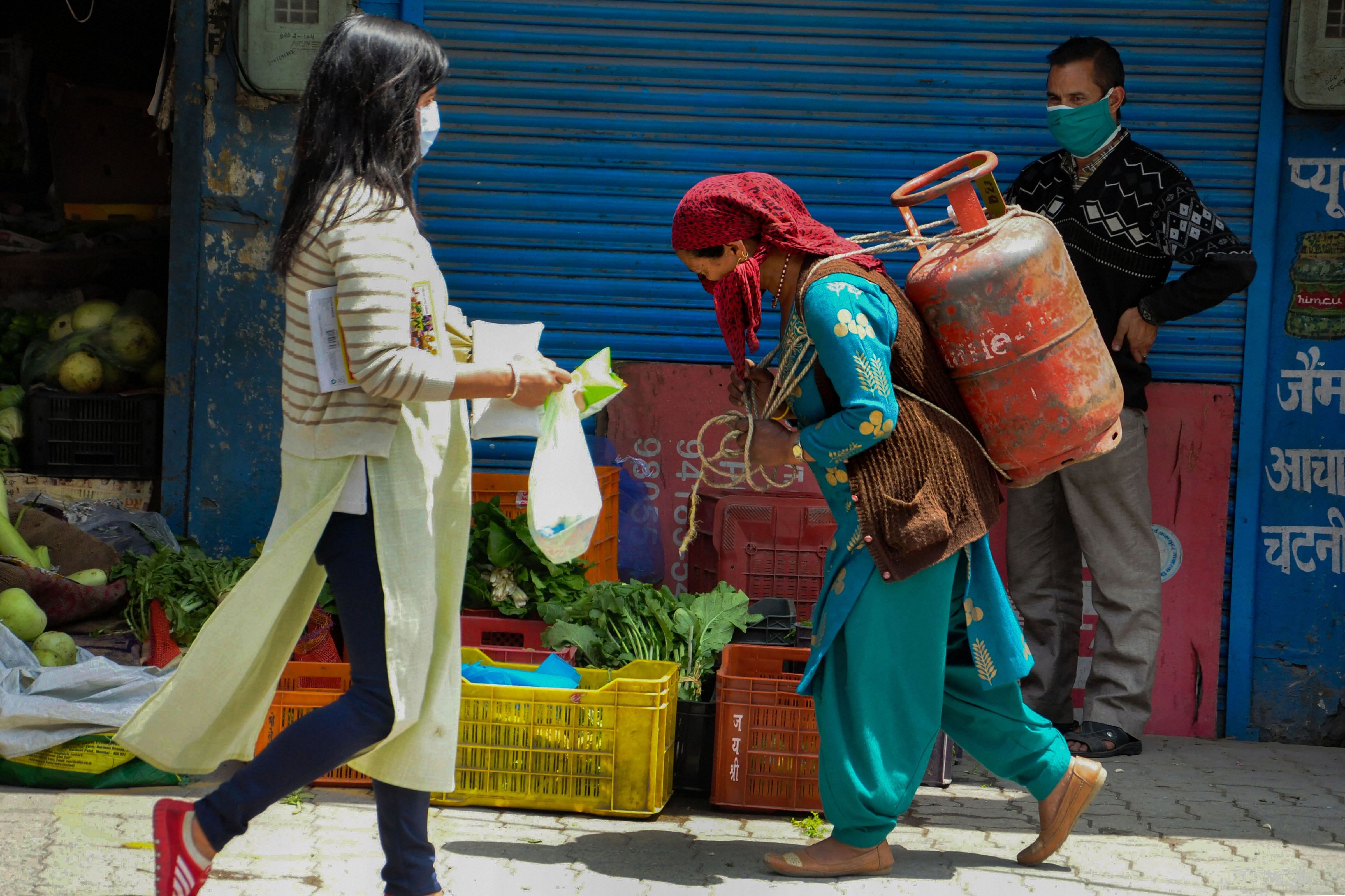 A woman carries a LPG cylinder on her back as another woman walks past her, during the nationwide lockdown to curb the spread of coronavirus. (PTI Photo)