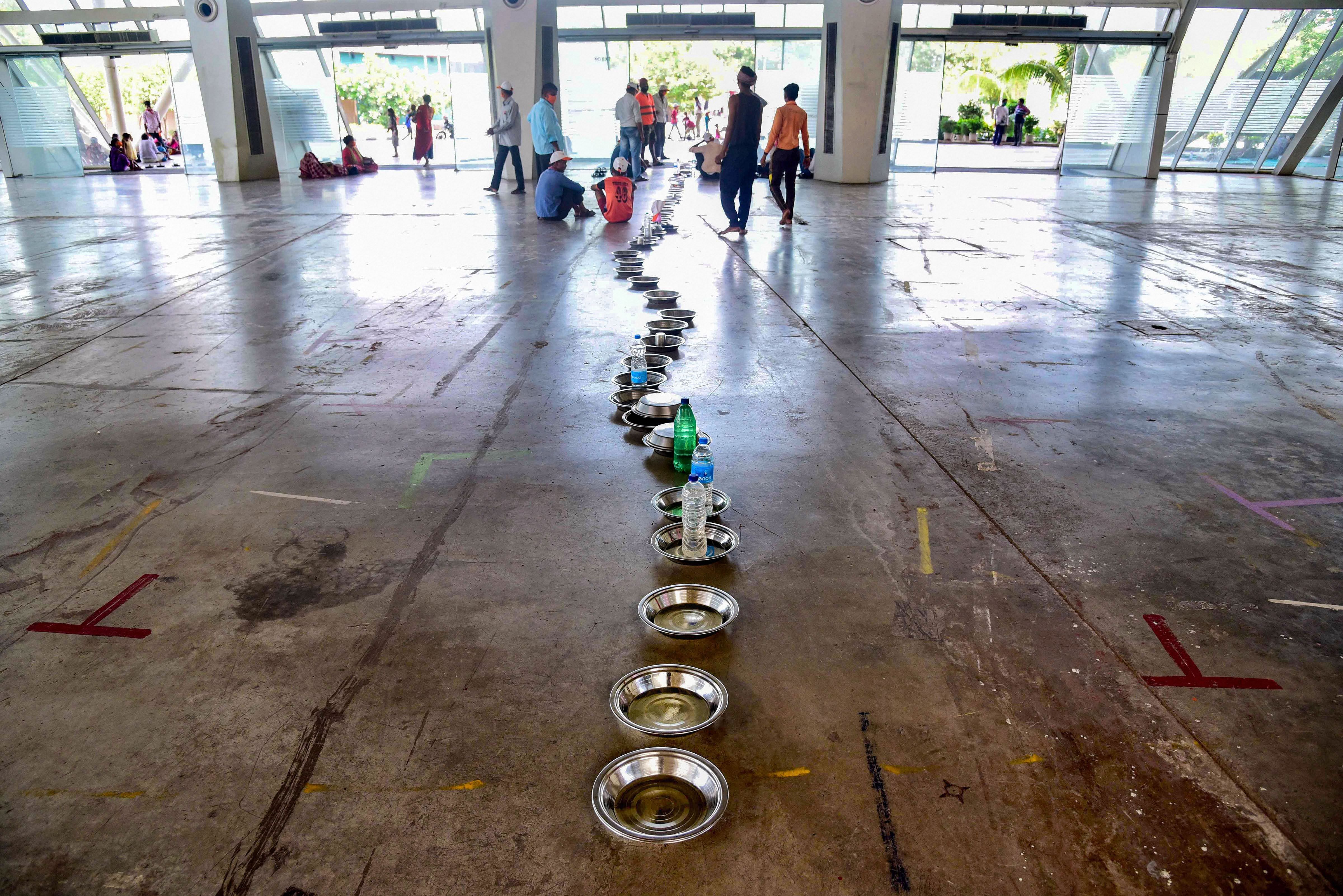Migrant workers keep their plates in a queue to reserve their spot ahead of food distribution at a government-run shelter home at CIDCO Exhibition Center, Vashi in Navi Mumbai. (PTI Photo)