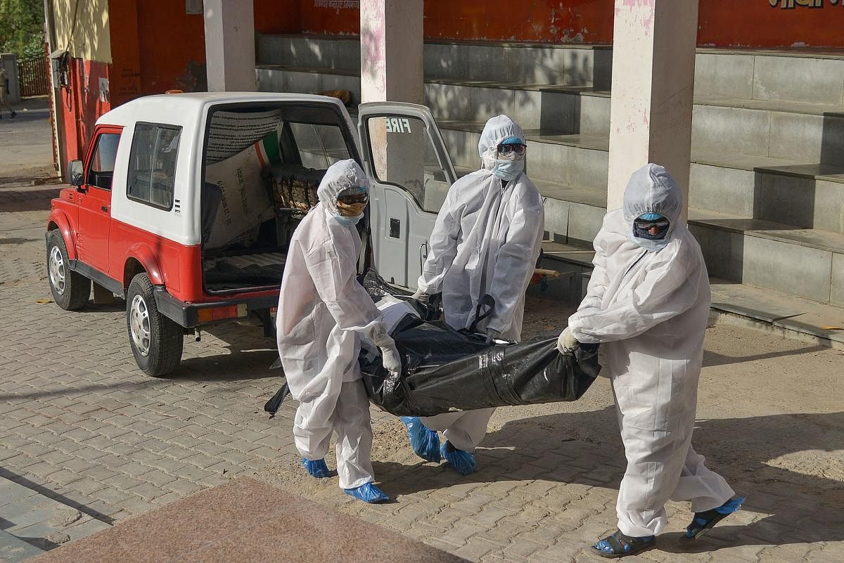 Health workers wearing protective gears hold the body of a victim of COVID-19 (AFP Photo)