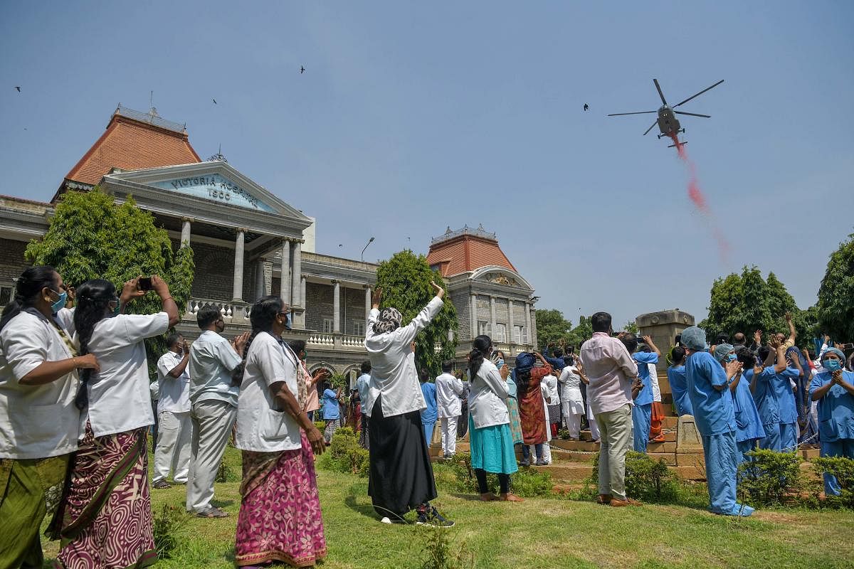 Medical staff and health workers cheer as an Indian Air Force (IAF) Mi-17 helicopter drops flower petals over the Victoria Hospital to pay tribute to 'frontline warriors' (AFP Photo)