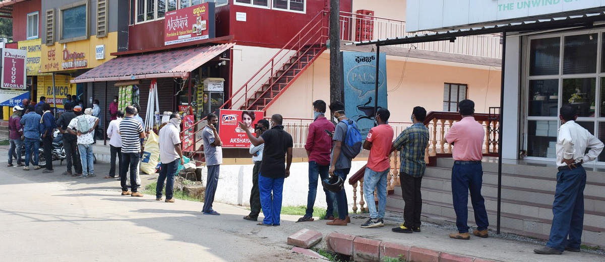 People queue up to buy alcohol in front of a shop in Madikeri on Monday. DH photo