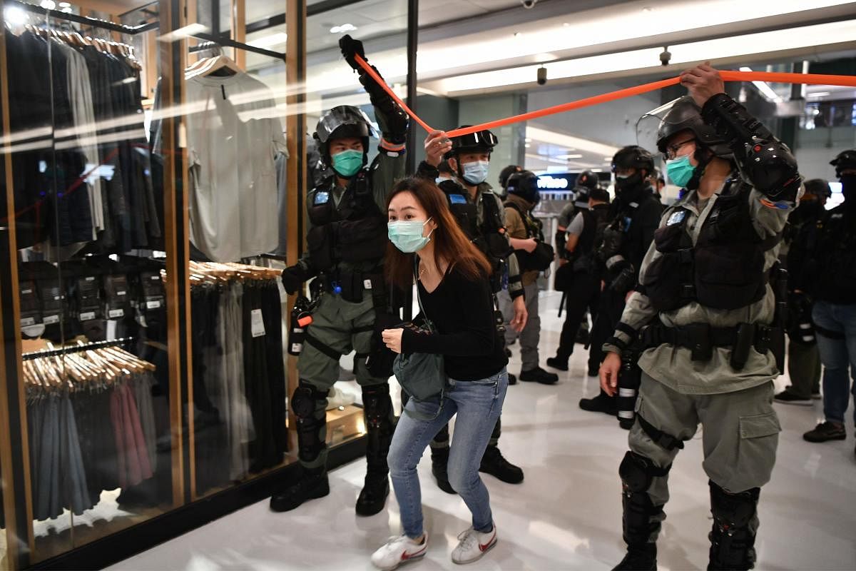A woman wears a face mask, as a precautionary measure against the COVID-19 coronavirus, as she walks under a cordon set up by riot police in a shopping mall during a protest by pro-democracy supporters (AFP Photo)