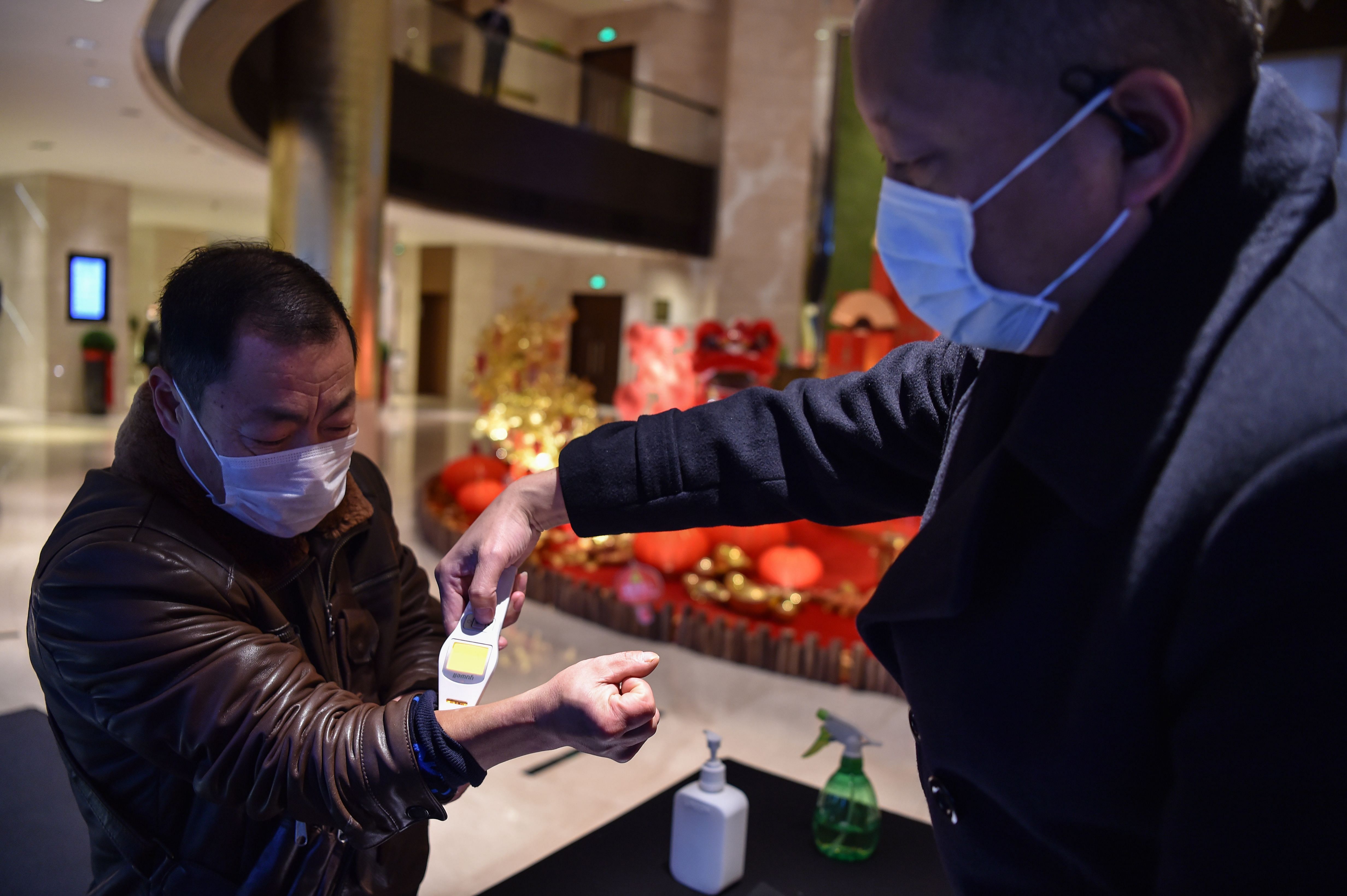 A hotel employee takes the temperature of a person that just arrived at the premise in Wuhan. (AFP Photo)