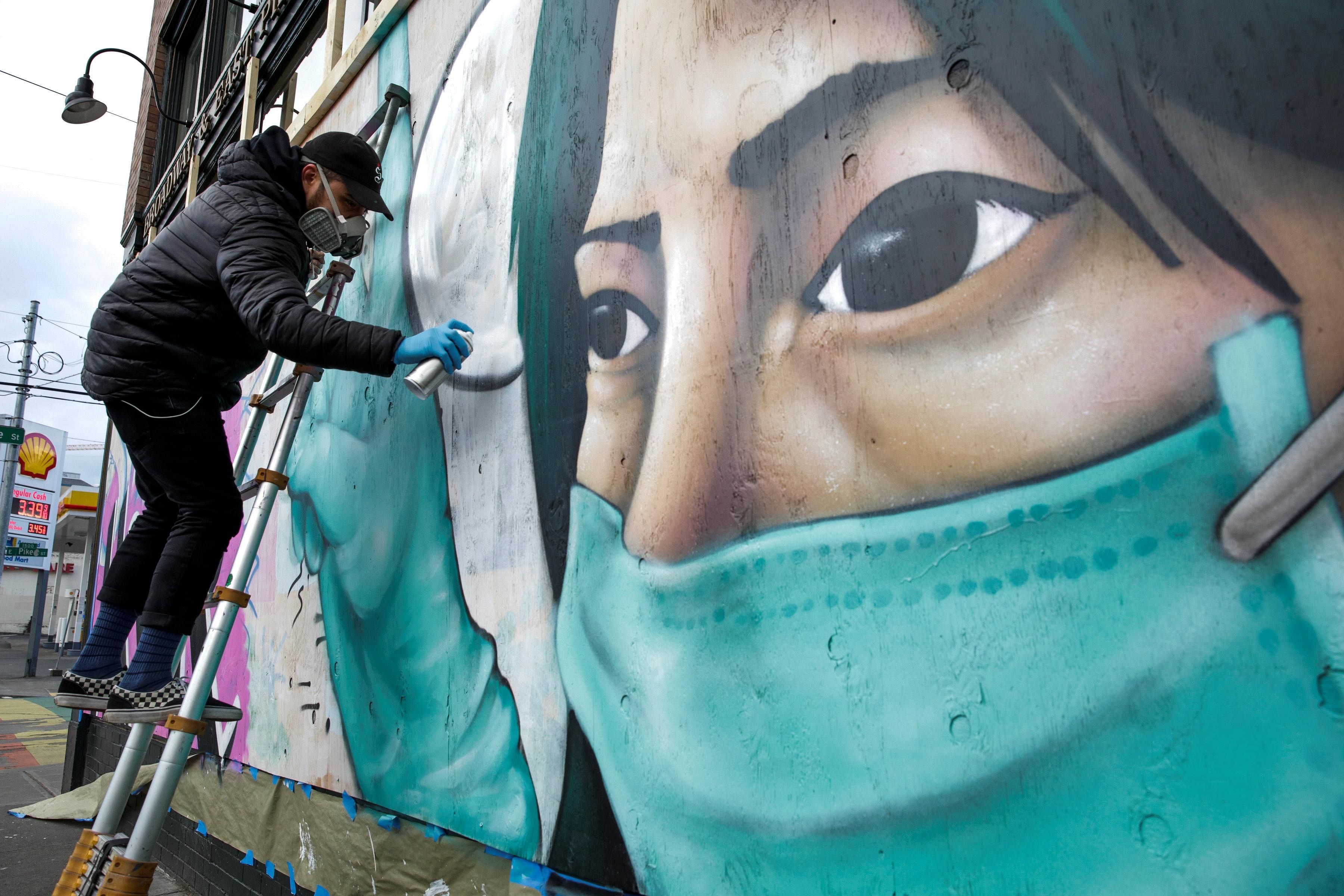 Street artist Carlos Giovanni, who goes by the name TheyDrift, works on the portrait of a healthcare worker for a piece he calls "Stay Home" in Seattle. (Credit: Reuters)