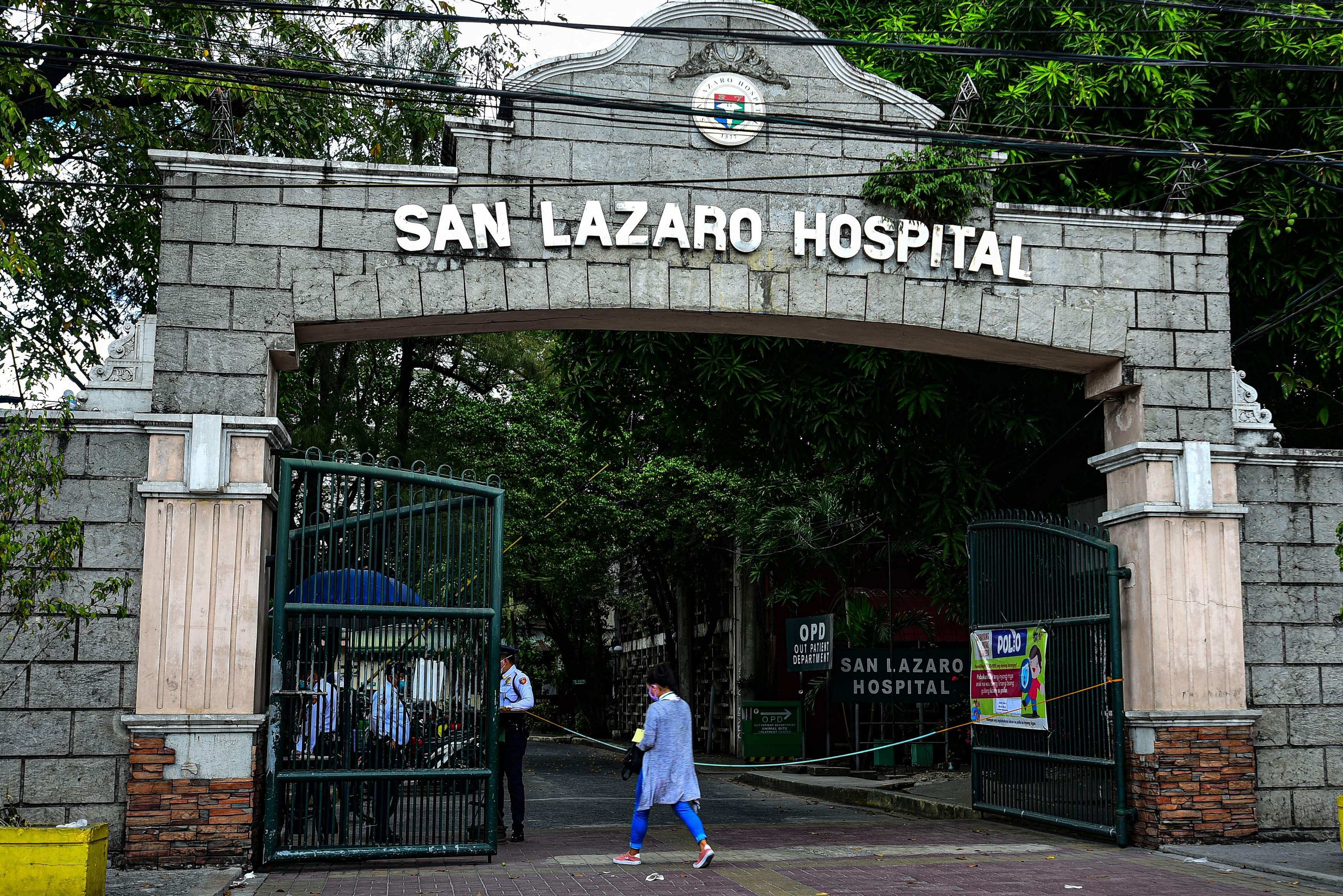 People wearing face masks walk past the main gates of the San Lazaro Hospital in Manila. (AFP Photo)