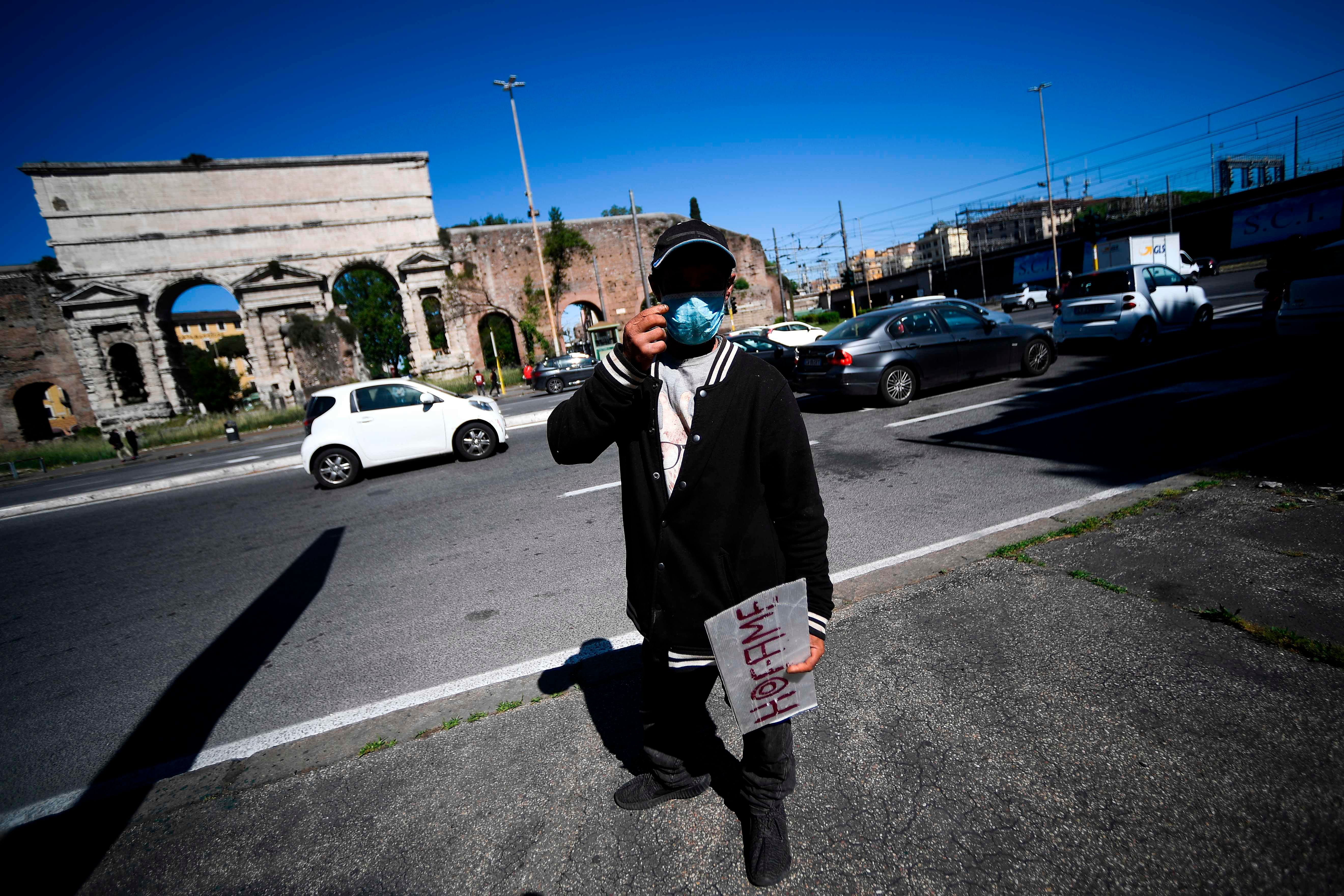 A homeless man stands by road traffic with a sign reading "I am hungry" at Porta Maggiore in Rome. (AFP Photo)