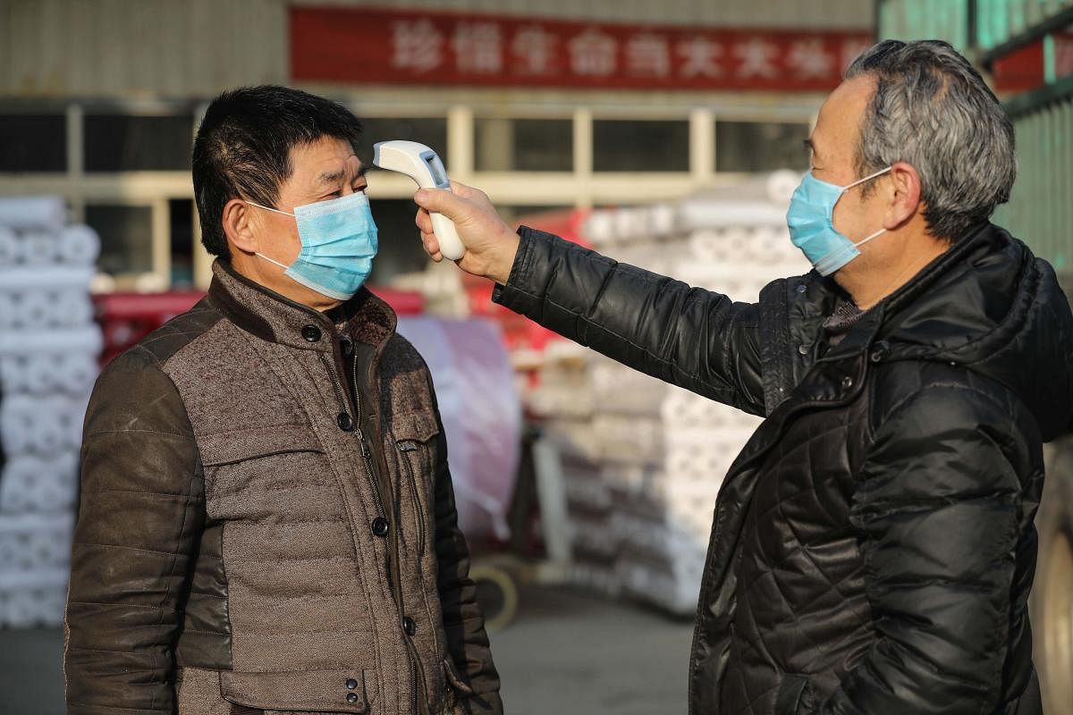 A worker checks the body temperature of a colleague at a textile factory in Hangzhou, in China's eastern Zhejiang province. (AFP Photo)