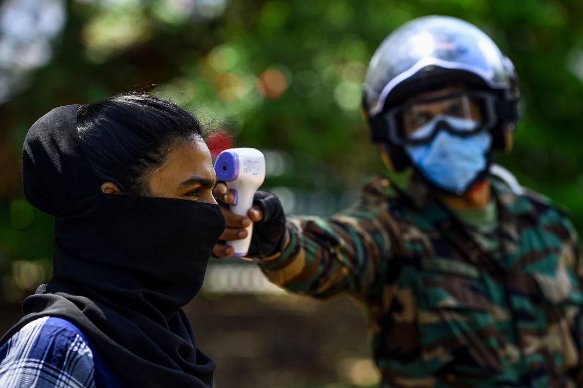 A security personnel (R) checks the body temperature of a pedestrian during a government-imposed nationwide lockdown as a preventive measure against the COVID-19 coronavirus, in Colombo on April 23, 2020. Credit: AFP Photo