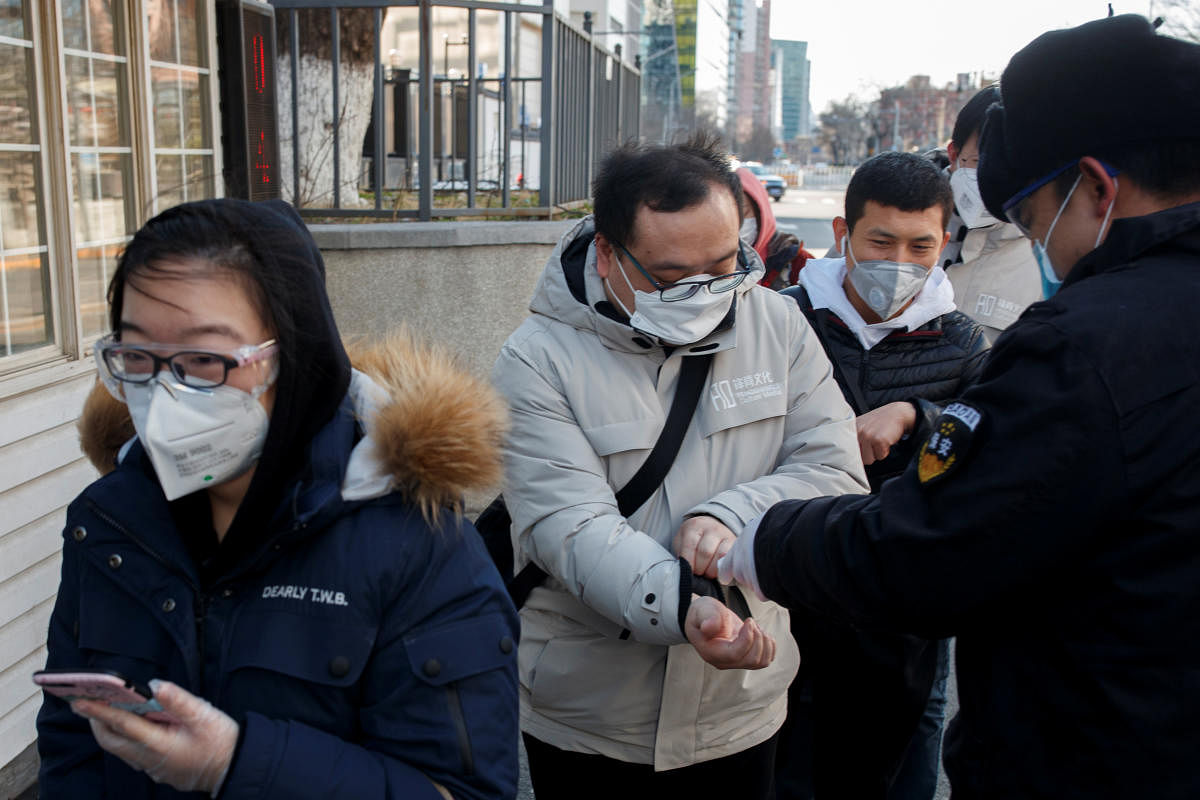 A security guard takes the temperature of people as they arrive for work at an office building in Beijing. (Reuters Photo)
