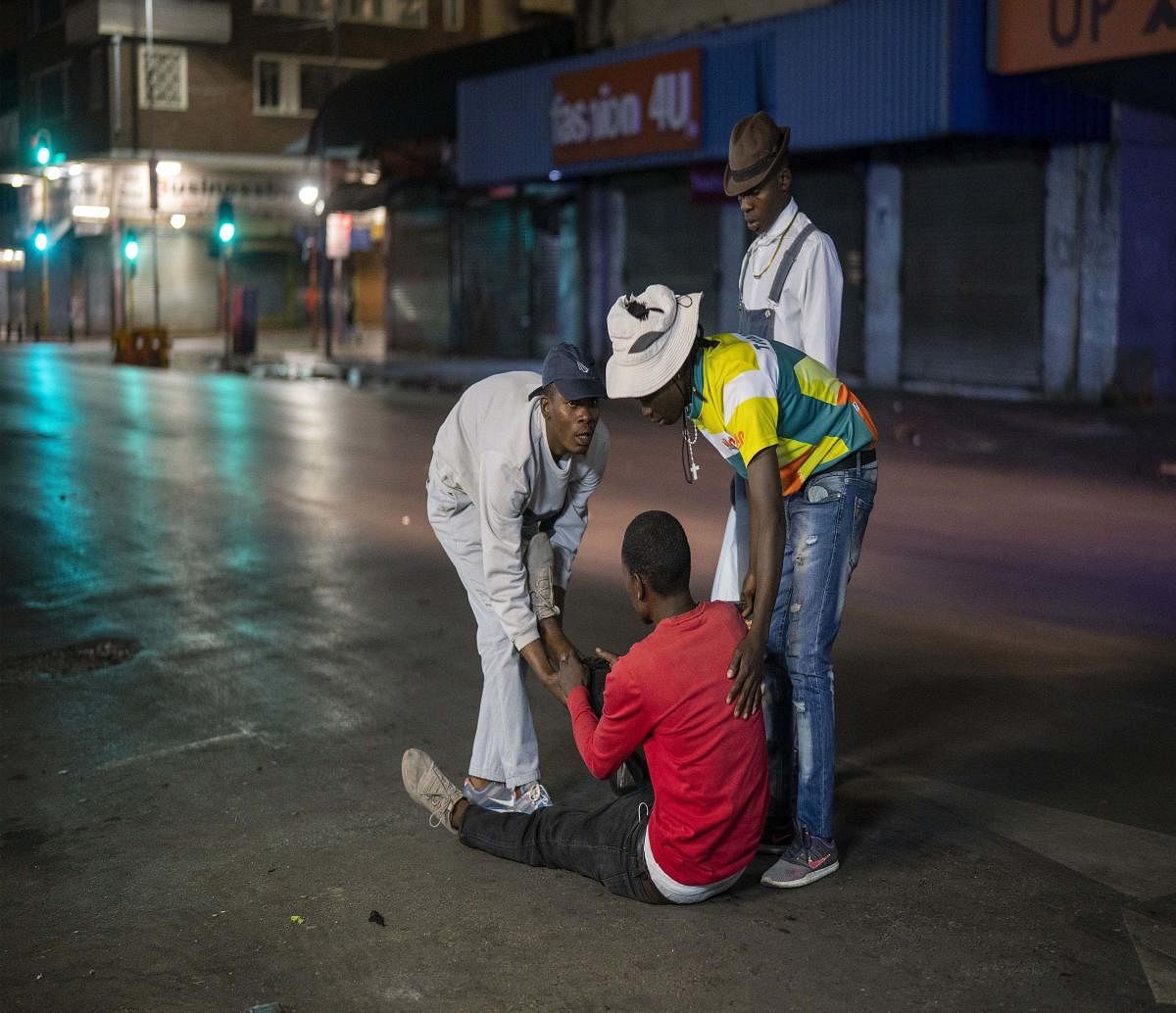 People assist a man who fell down after being chased by police for violating the lockdown in downtown Johannesburg, South Africa (AP Photo)