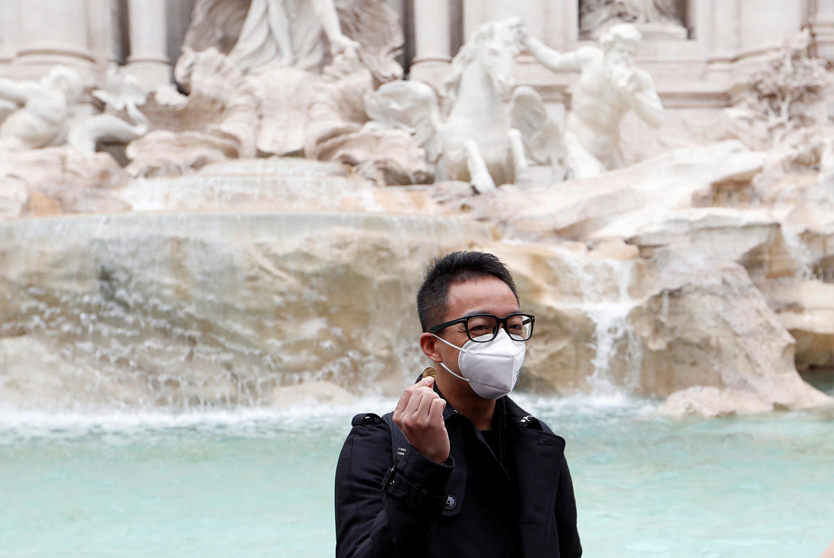 A tourist wearing protective masks waits to throw a coin to the Trevi's Fountain after two cases of coronavirus were confirmed in Italy. Reuters