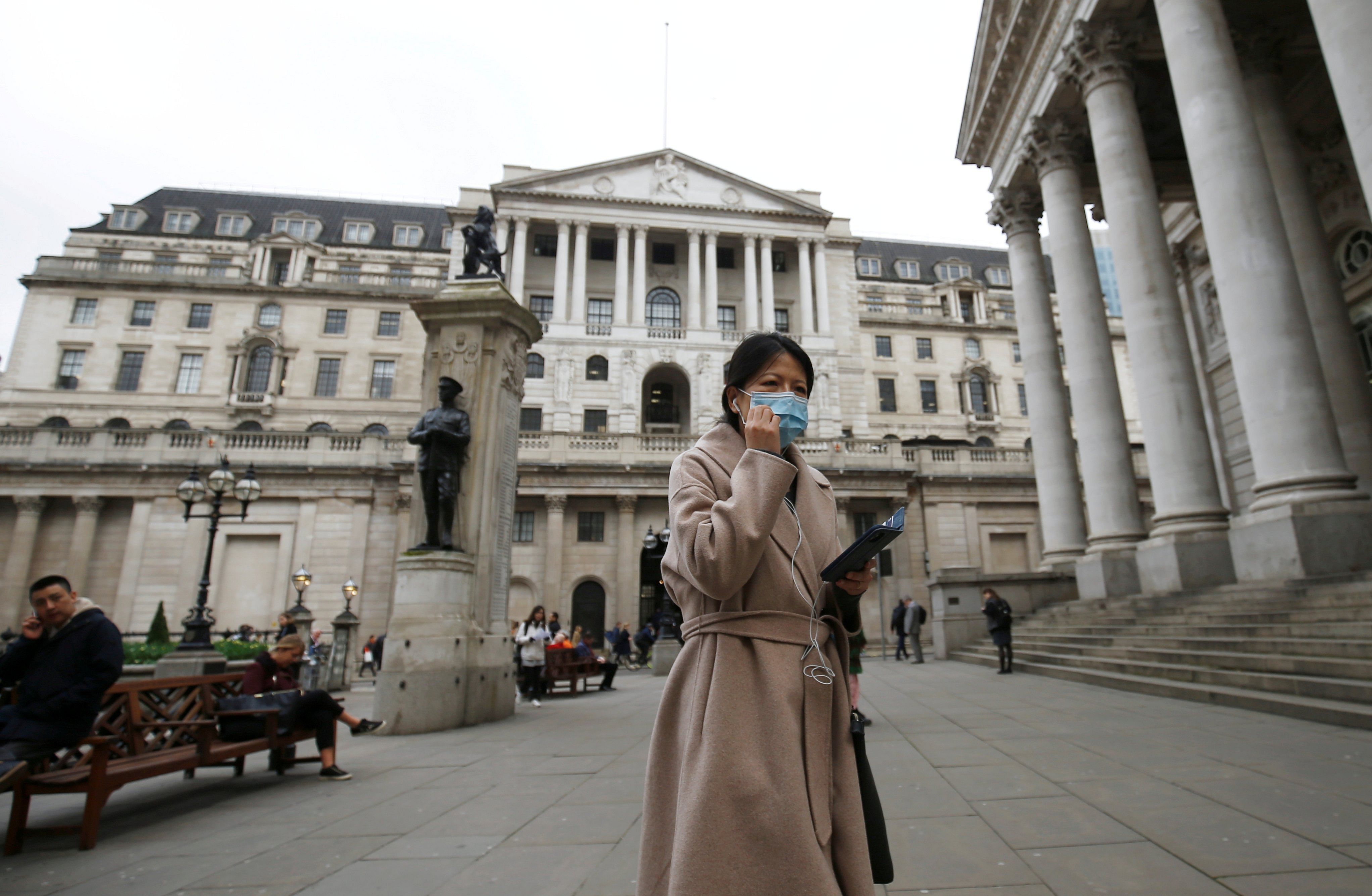 A woman, wearing a protective face mask, walks in front of the Bank of England, following an outbreak of the coronavirus, in London. (Credit: Reuters)