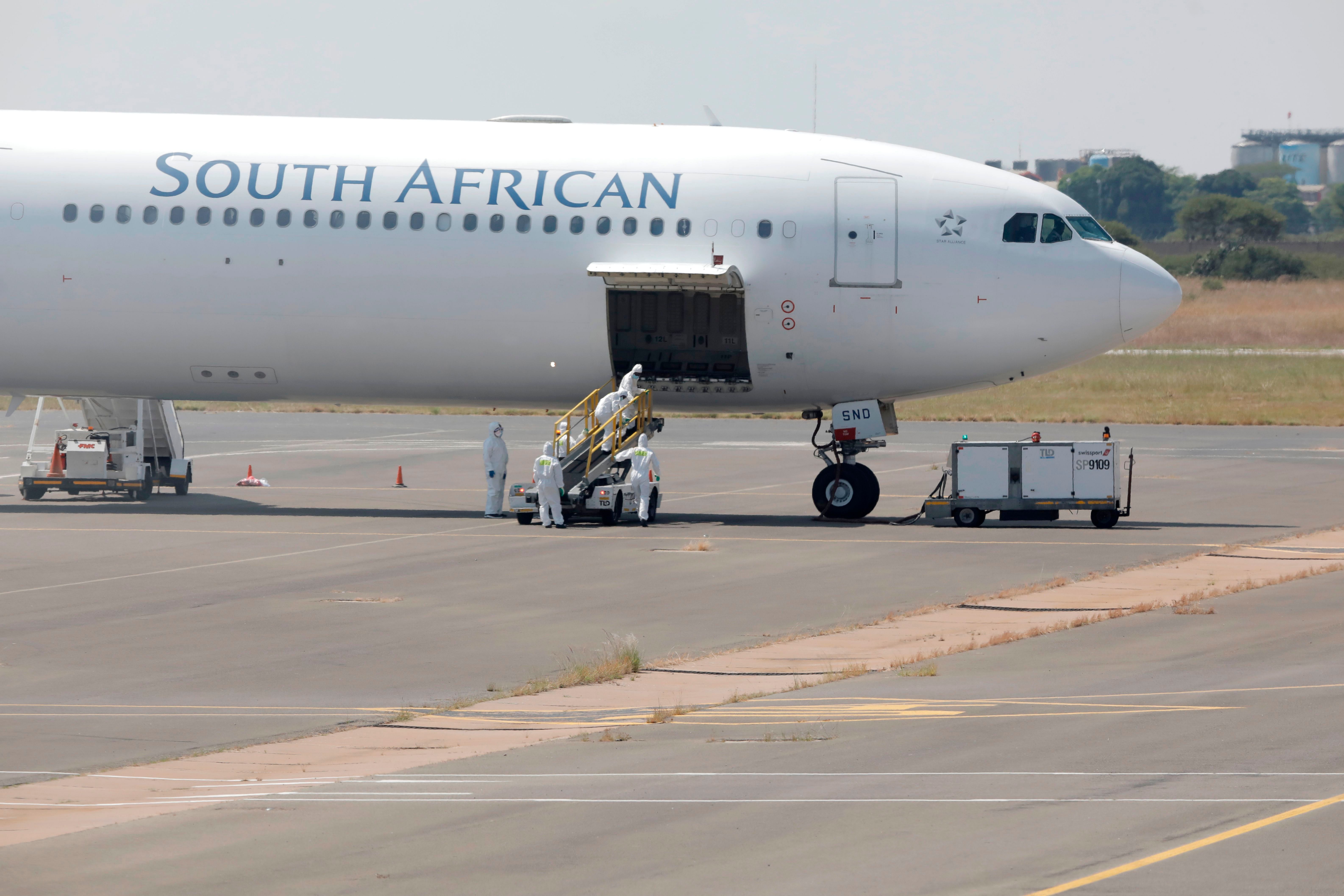 Workers wearing protective suit approach a South African Airways Airbus A340-600 plane on March 14, 2020 as it arrives in Johannesburg, carrying South African citizens who have been repatriated from Wuhan, China.(Credit: AFP Photo)