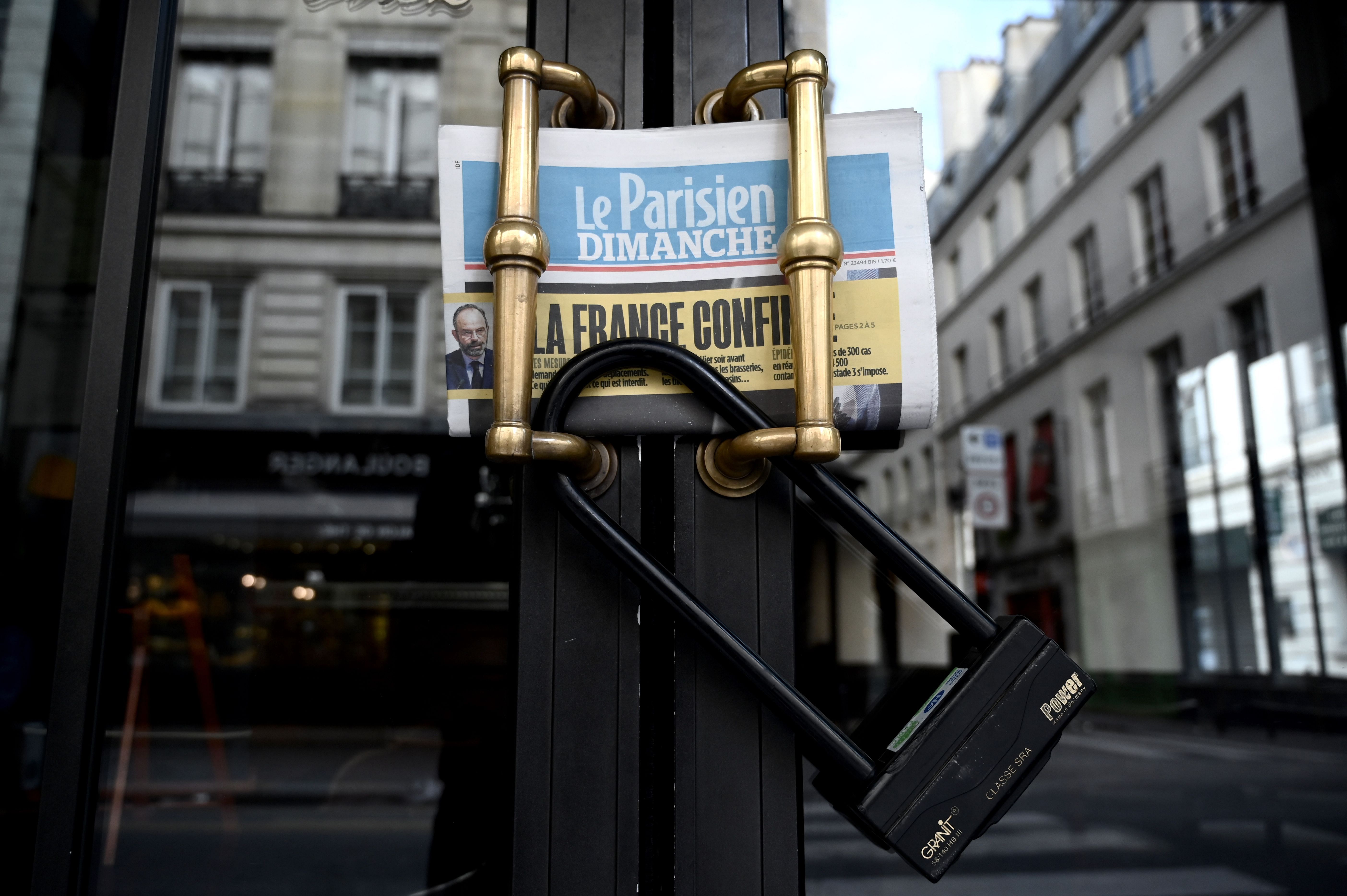 A picture taken on March 15, 2020 in Paris shows the closed entrance door of a cafe and the Parisien daily newspaper reading "France confined" (Credit: AFP)