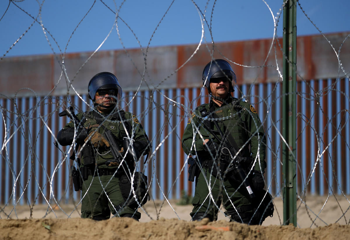 Members of a US border patrol stand near the border fence between Mexico and the United States as migrants stand near by in Tijuana, Mexico, November 25, 2018. (REUTERS)