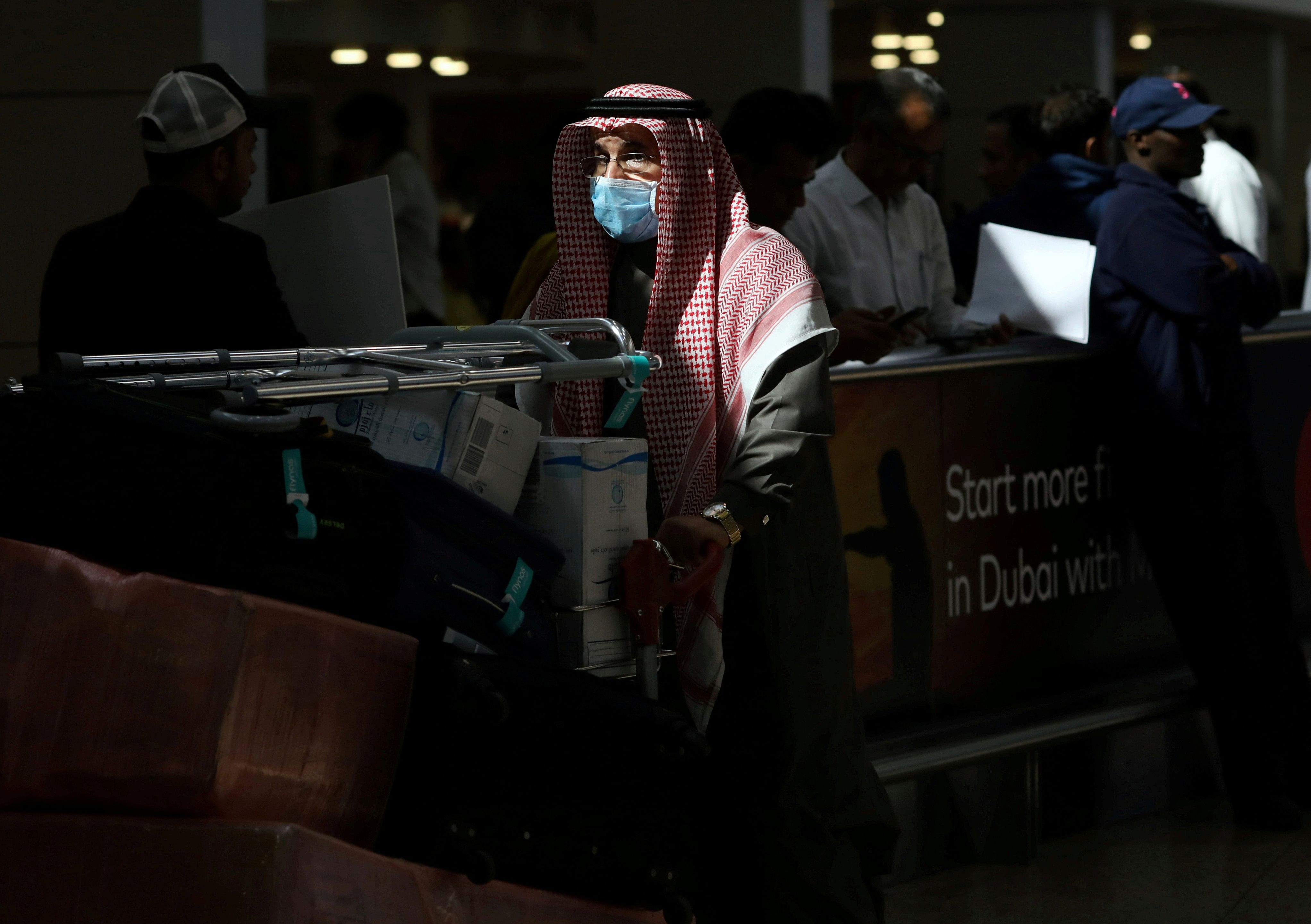 A traveller wears a mask as he pushes a cart with luggage at Dubai International Airport. (Credit: Reuters)