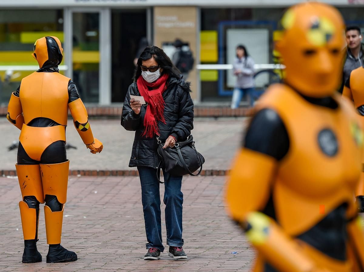 A woman wearing a protective face mask as a precaution against the spread of the new coronavirus, the COVID-19, walks by traffic personnel on road safety robot suits, in Bogota on March 6, 2020. Credit: AFP Photo