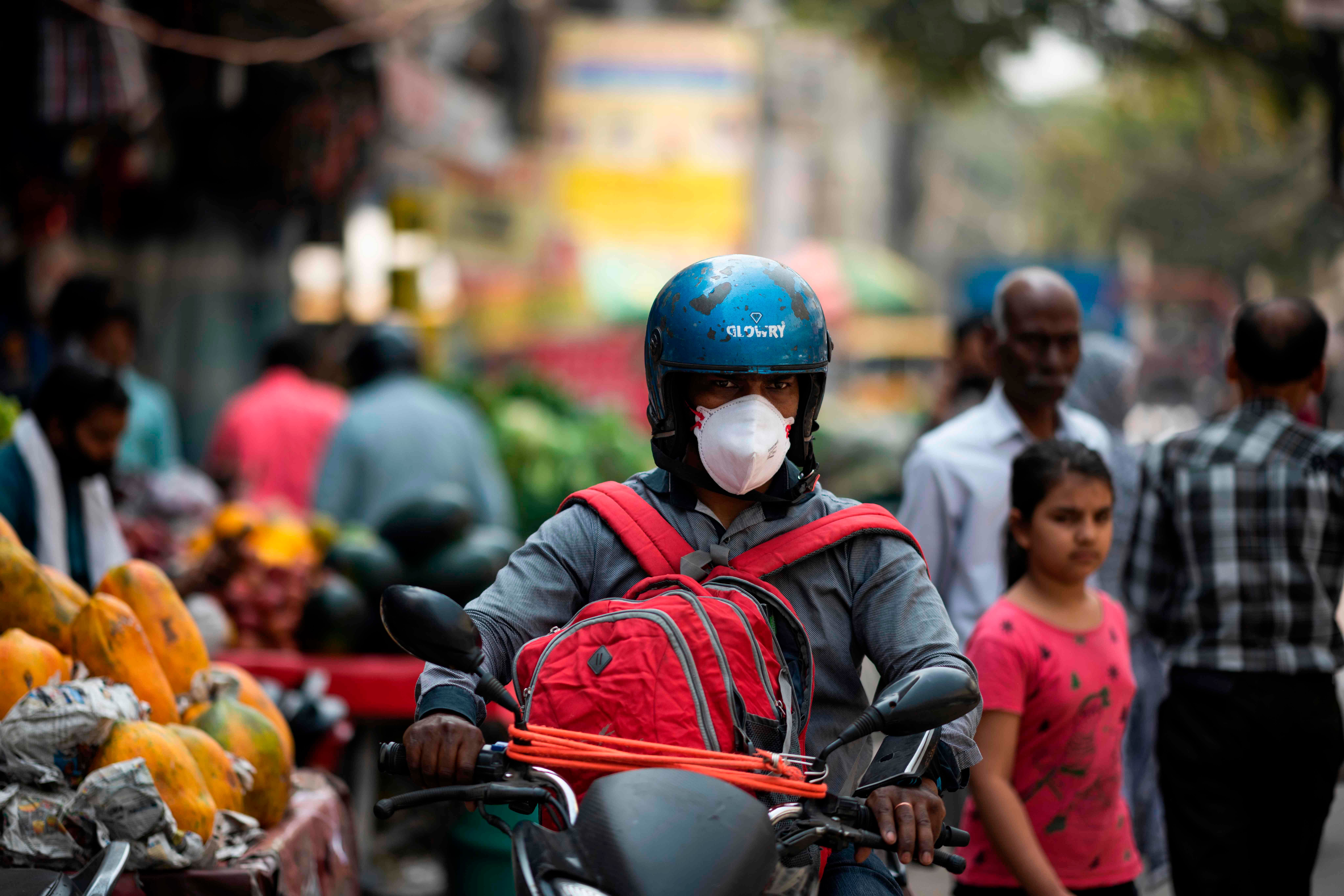 A man (C) wearing a facemask as a preventive measure against the COVID-19 coronavirus rides a motorbike along a street in New Delhi. (AFP Photo)