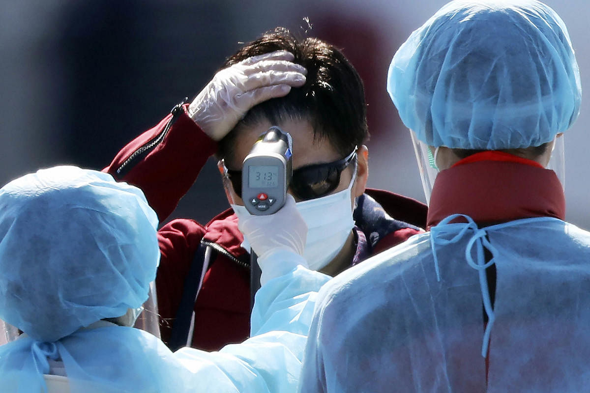 An official in protective suits measure the temperature of the foreign passengers disembarked from the quarantined ship (AP Photo)