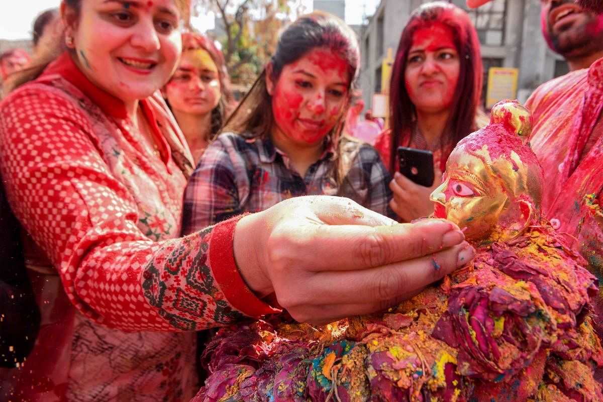 Hindu devotees put coloured powder on an idol of deity Lord Krishna (R) during Holi (AFP Photo)