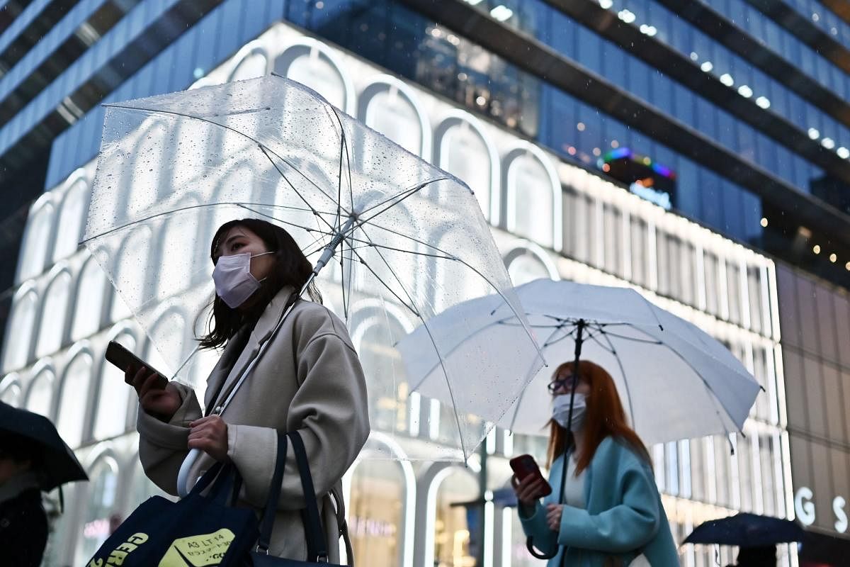 Women wearing face masks hold umbrellas as they walk down a street in the rain in Tokyo's Ginza area on March 10, 2020. (Photo by CHARLY TRIBALLEAU / AFP)