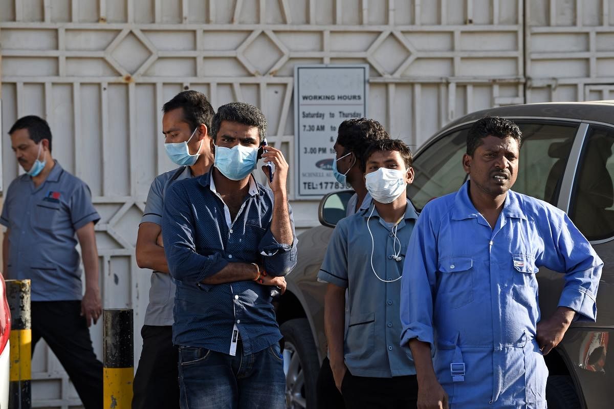 Foreign workers watch as Bahraini policemen seal off a building in the Salmabad industrial area as a precautionary measure after a resident tested positive for coronavirus (COVID-19), on the outskirts of the capital Manama on March 13, 2020. (Photo by Mazen Mahdi / AFP)