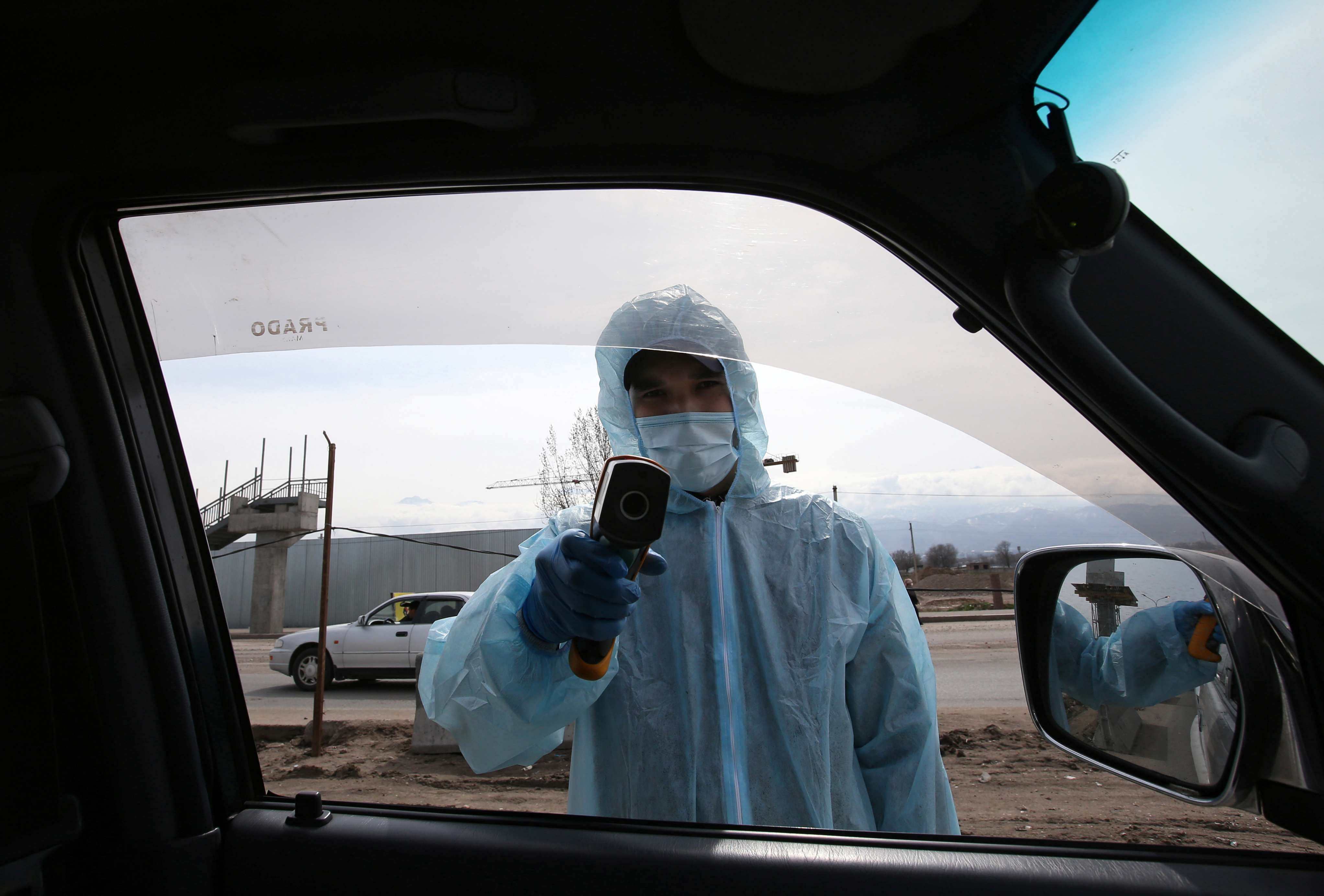 A medical official wearing protective gear takes the body temperature of passengers at a checkpoint set up to lock down the city to prevent the spread of coronavirus disease (COVID-19), on the outskirts of Almaty, Kazakhstan. (Credit: Reuters)