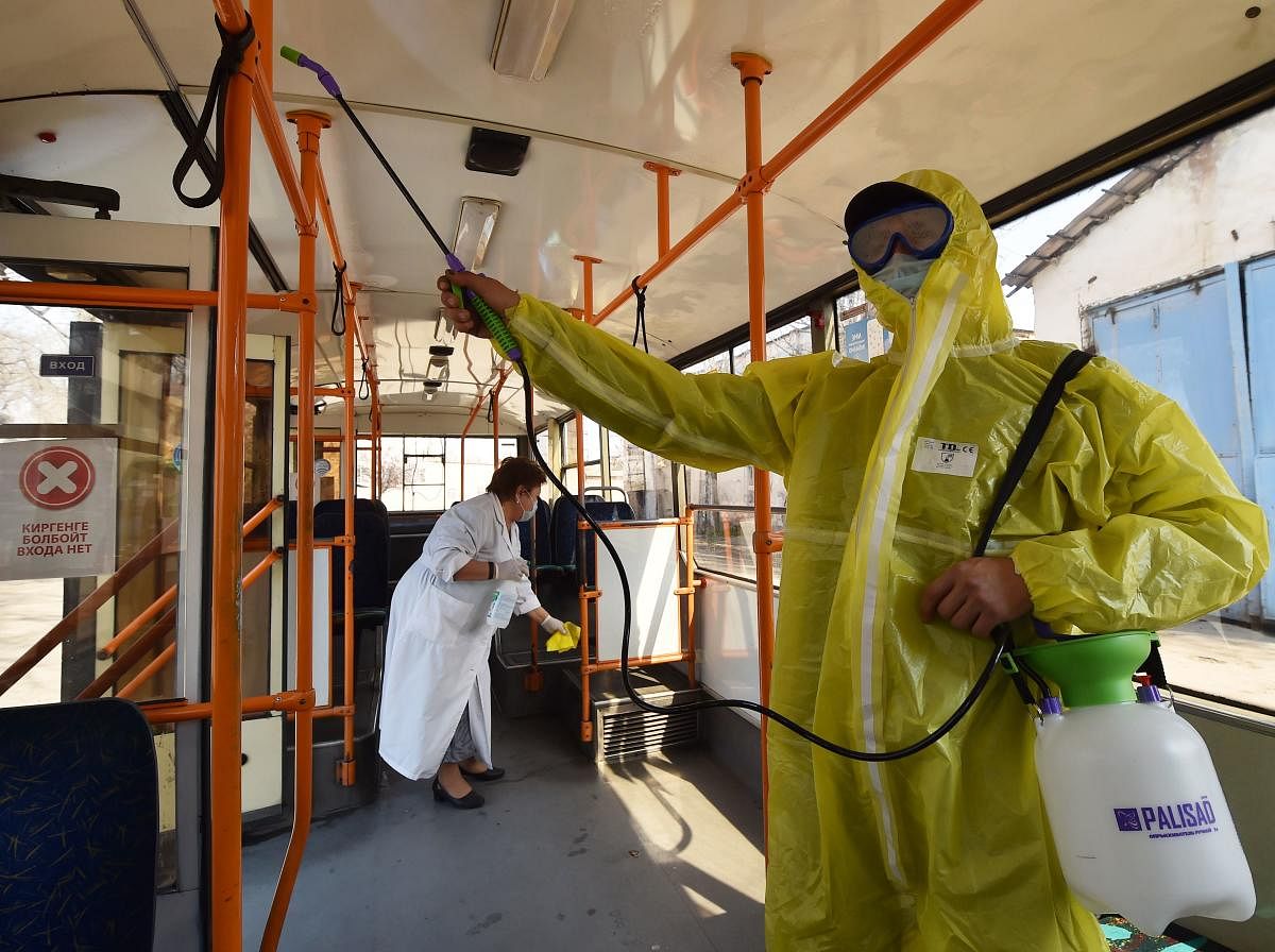 An employee wearing protective gear sprays disinfectant inside a trolleybus - as part of preventive measures against the COVID-19 coronavirus - in Bishkek (AFP Photo)