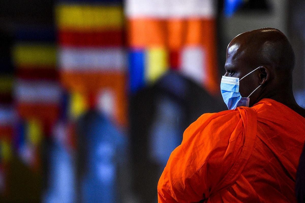 A Buddhist monk wearing a facemask amid concerns over the spread of the COVID-19 novel coronavirus stands at the Temple of the Sacred Tooth Relic in Kandy on March 18, 2020. Credit: AFP Photo