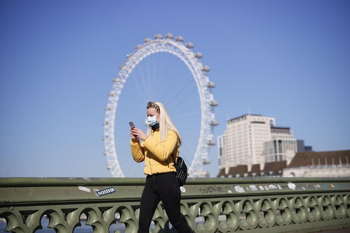 A pedestrian in a mask walks along Westminster Bridge with the London Eye in the backgroud, in a quiet central London (AFP Photo)