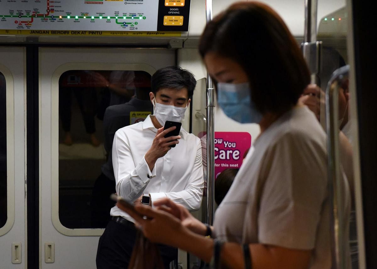 Commuters wearing face masks as a preventive measure against the COVID-19 coronavirus look at their mobile phones on the Mass Rapid Transit train in Singapore on March 18, 2020. Credit: AFP Photo