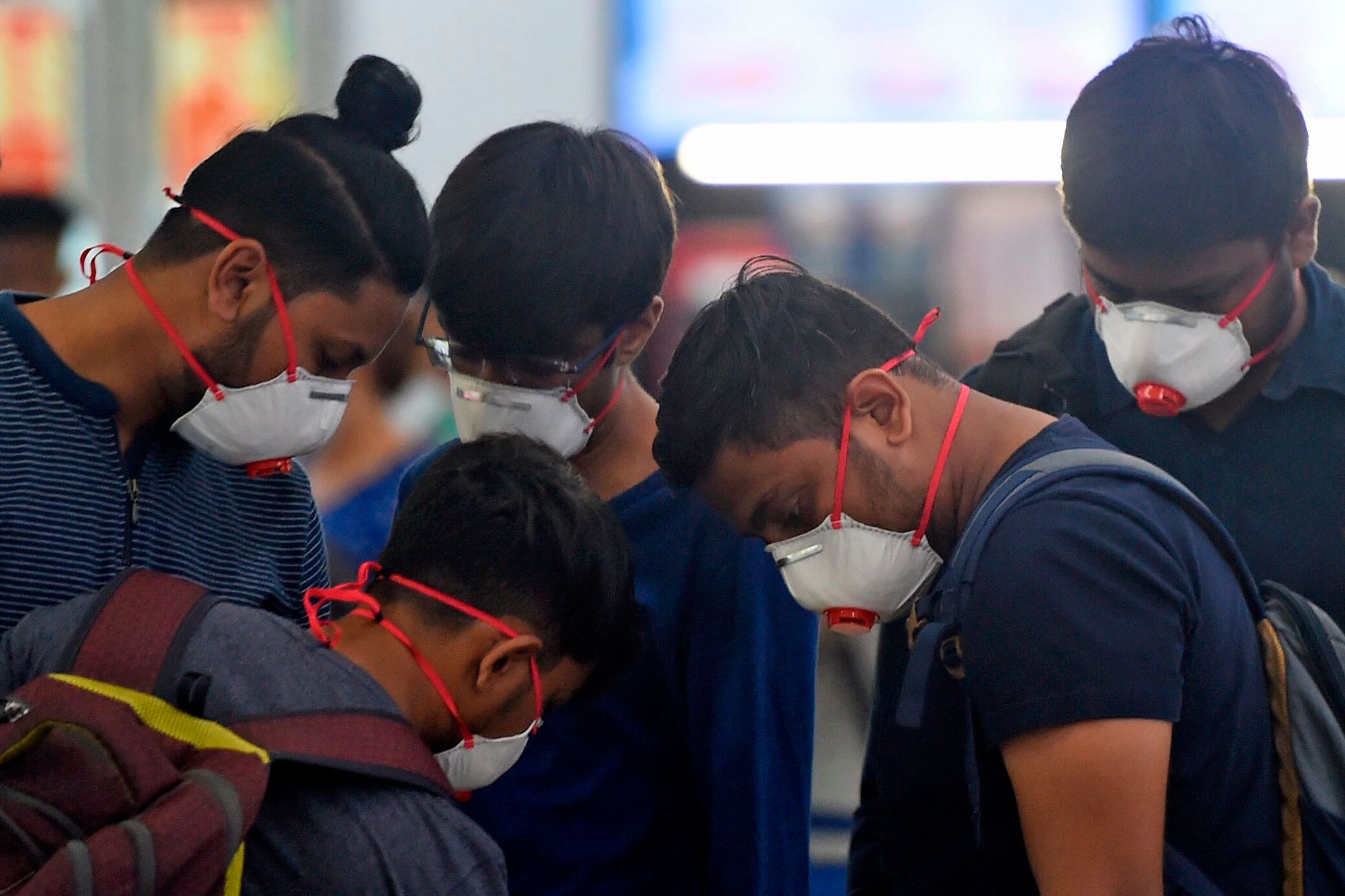 Passengers wearing facemasks amid concerns over the spread of the COVID-19 novel coronavirus, stand in a queue at a counter inside the airport in Goa