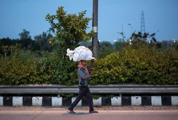 A migrant worker carries his belongings as he walks along a road to return to his village, during a 21-day nationwide lockdown to limit the spreading of coronavirus disease, in New Delhi. (Credit: Reuters Photo)