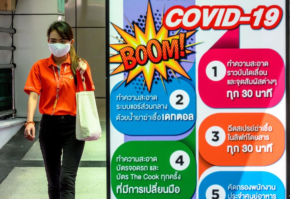 A woman, wearing a face mask as a preventive measure against the spread of the COVID-19 novel coronavirus, walks next to an information board about how to reduce the spread of the virus in Bangkok on March 27, 2020. (Photo by Mladen ANTONOV / AFP)