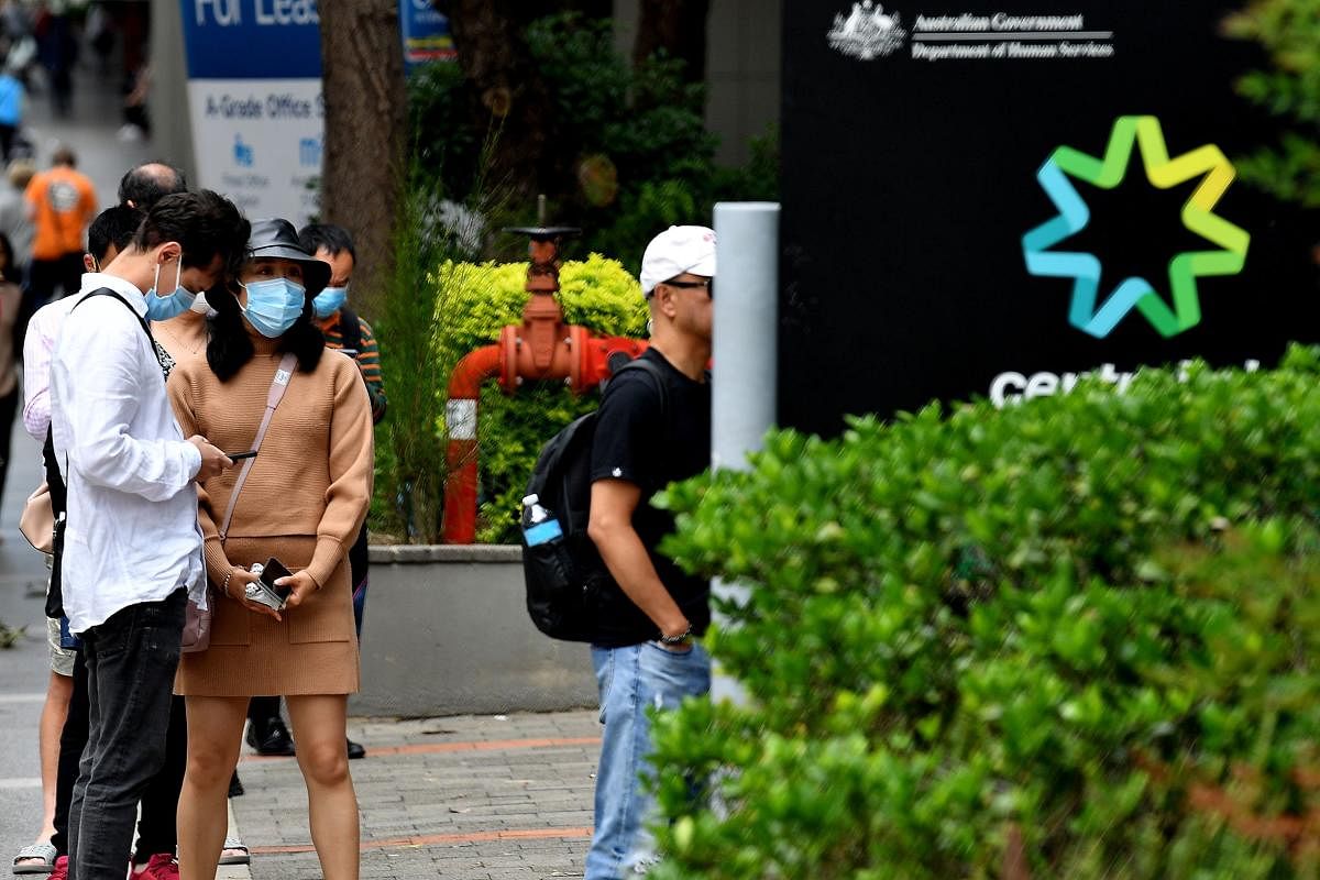 People wait in a queue to receive benefit payouts, including unemployment and small business support as the novel coronavirus inflicts a toll on the economy. AFP